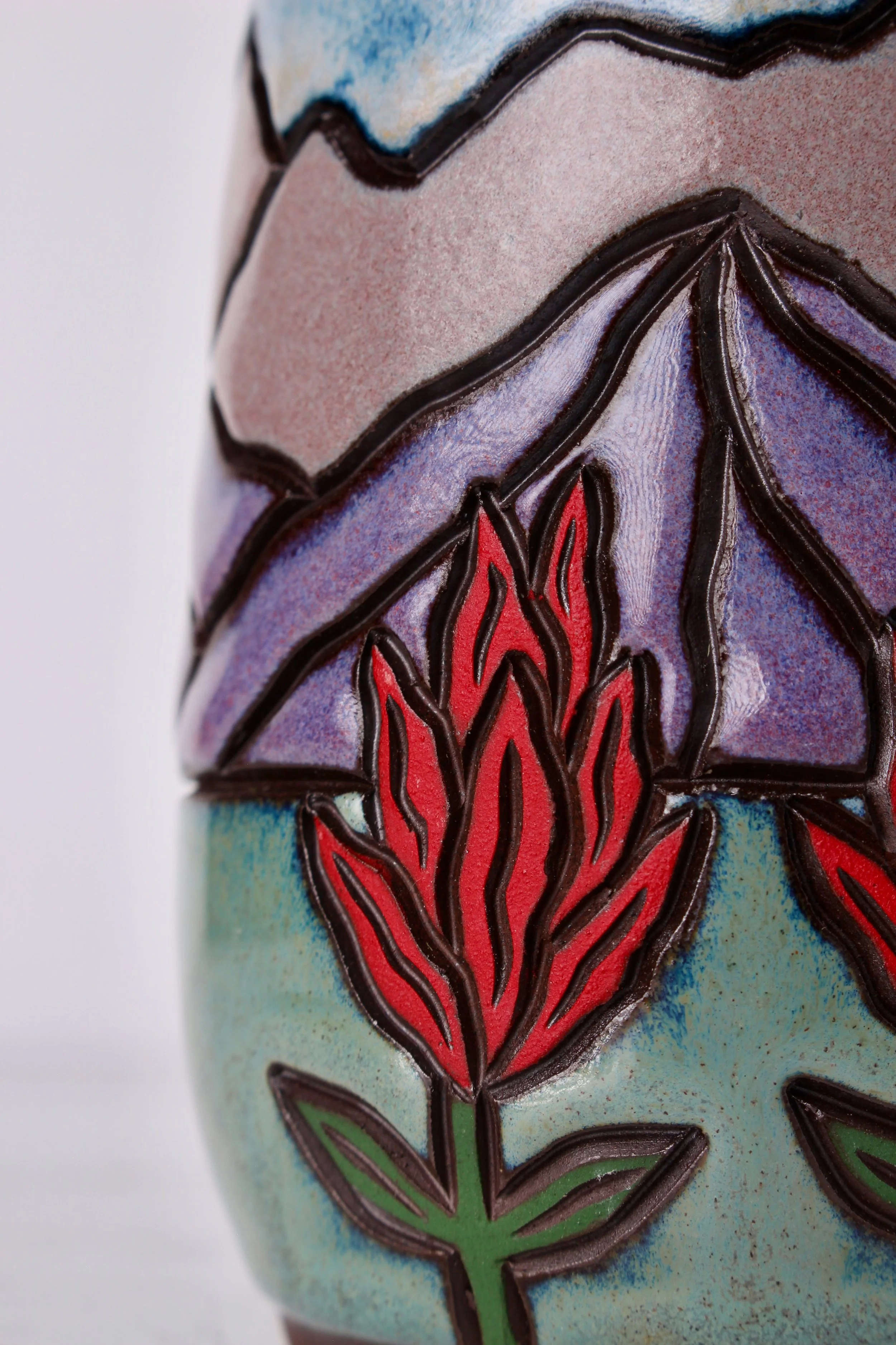 Close-up of a painted design on a unique shaped ceramic or clay object, featuring a red floral pattern and green leaves, outlined in black.