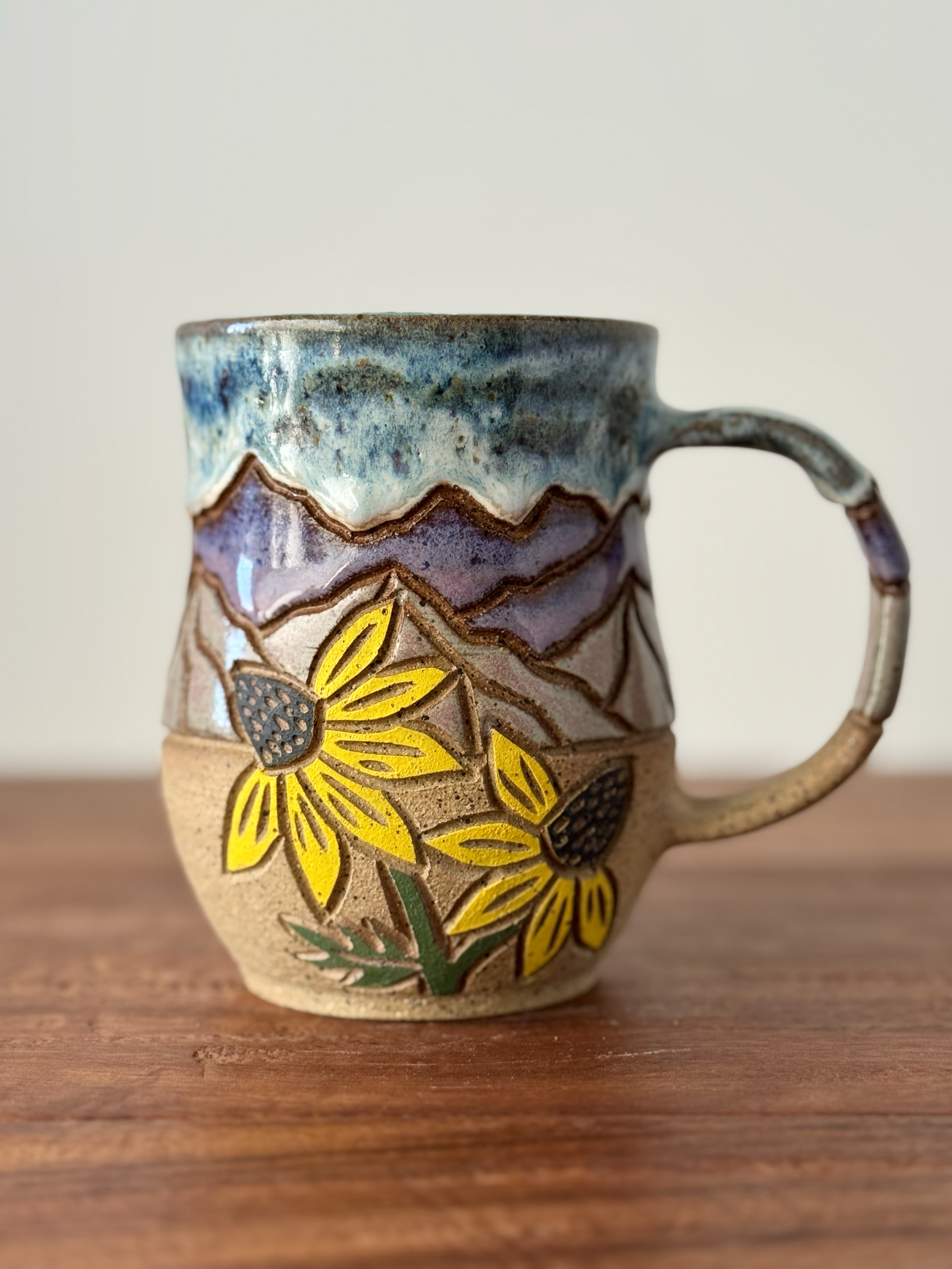 Close-up of a handmade ceramic mug with sunflower design, sitting on a wooden surface.