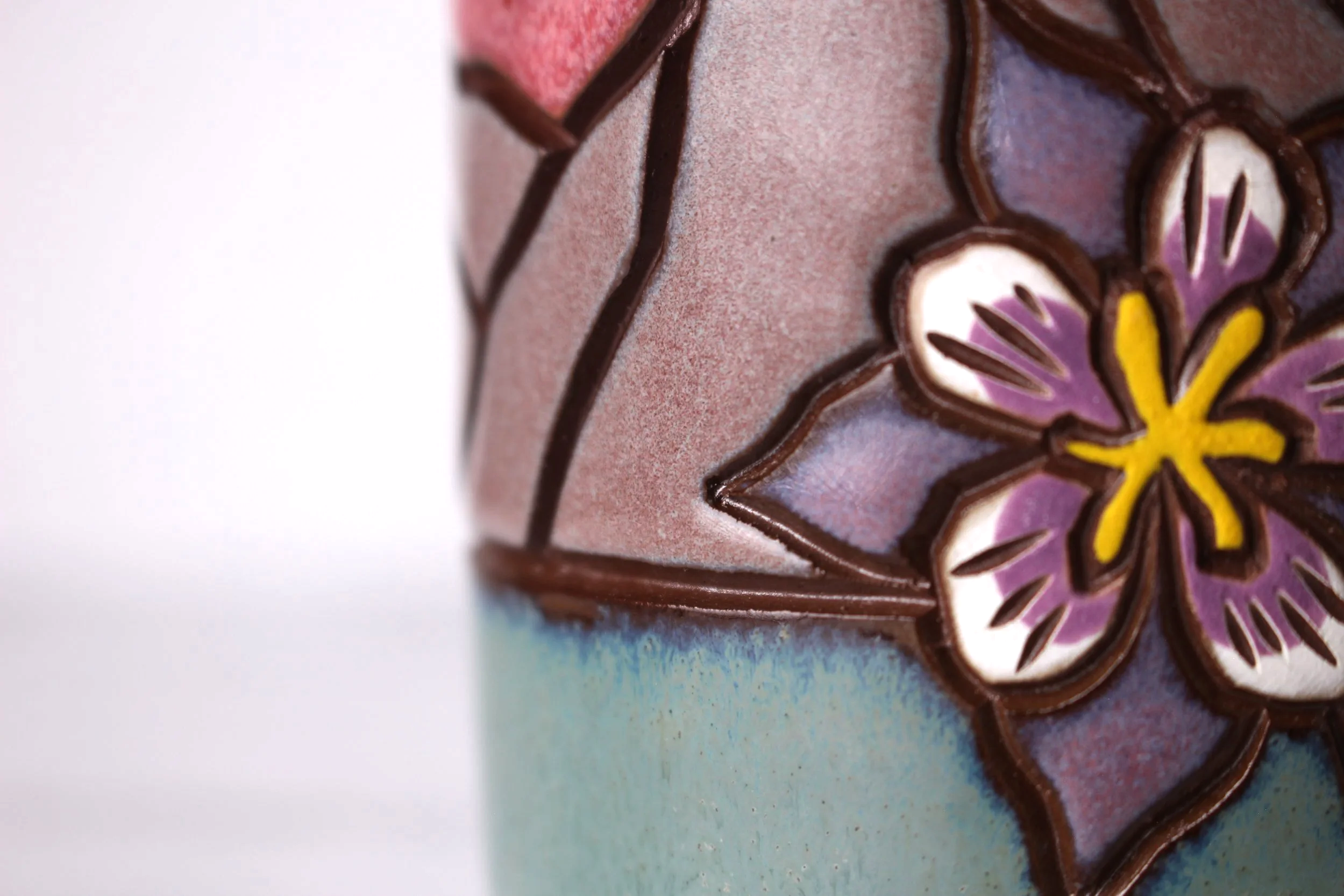 Close-up of carved flower on ceramics with purple, yellow, and white glaze on a white background.
