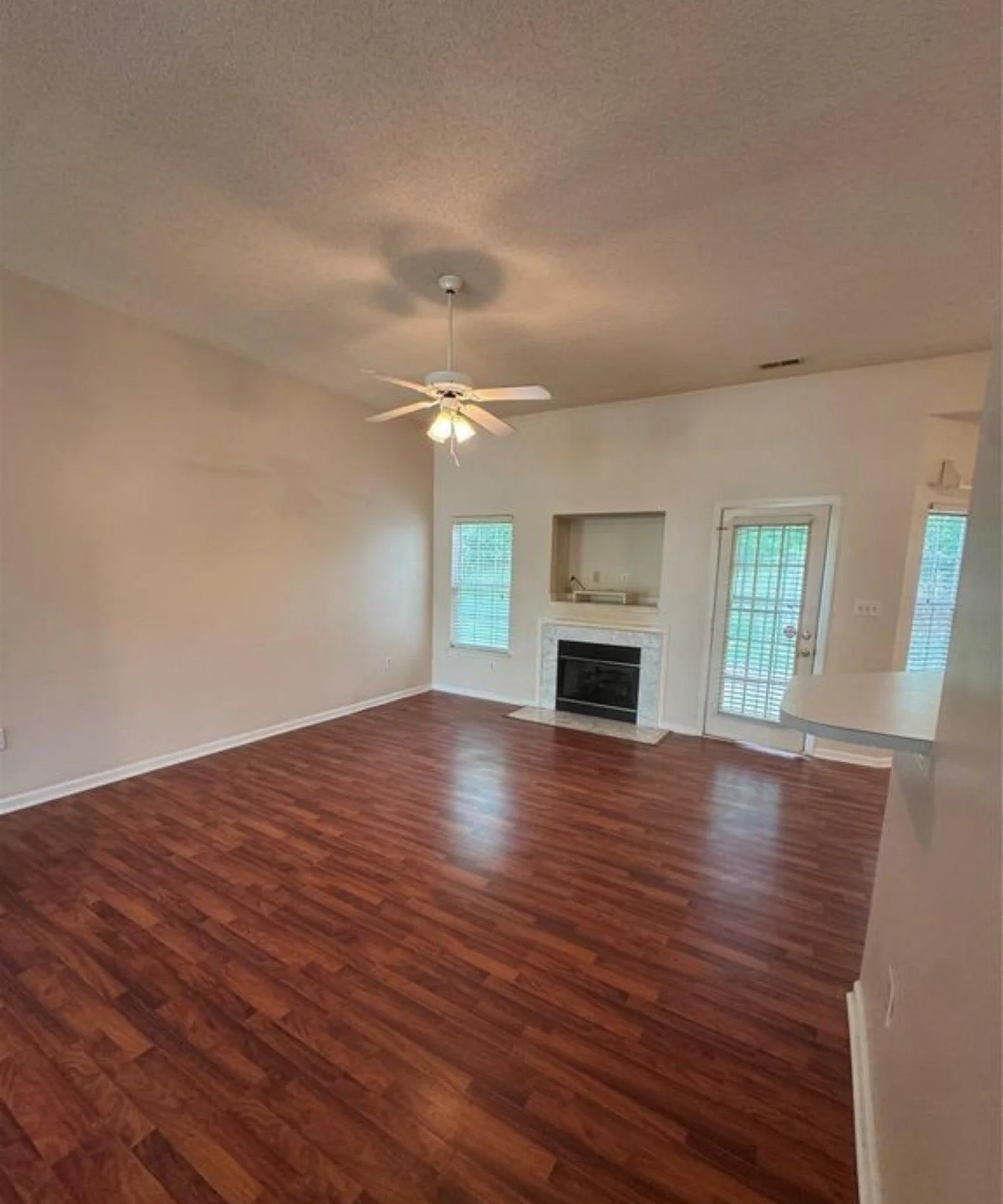 Empty living room with hardwood floors, a ceiling fan, a fireplace, and windows with blinds.