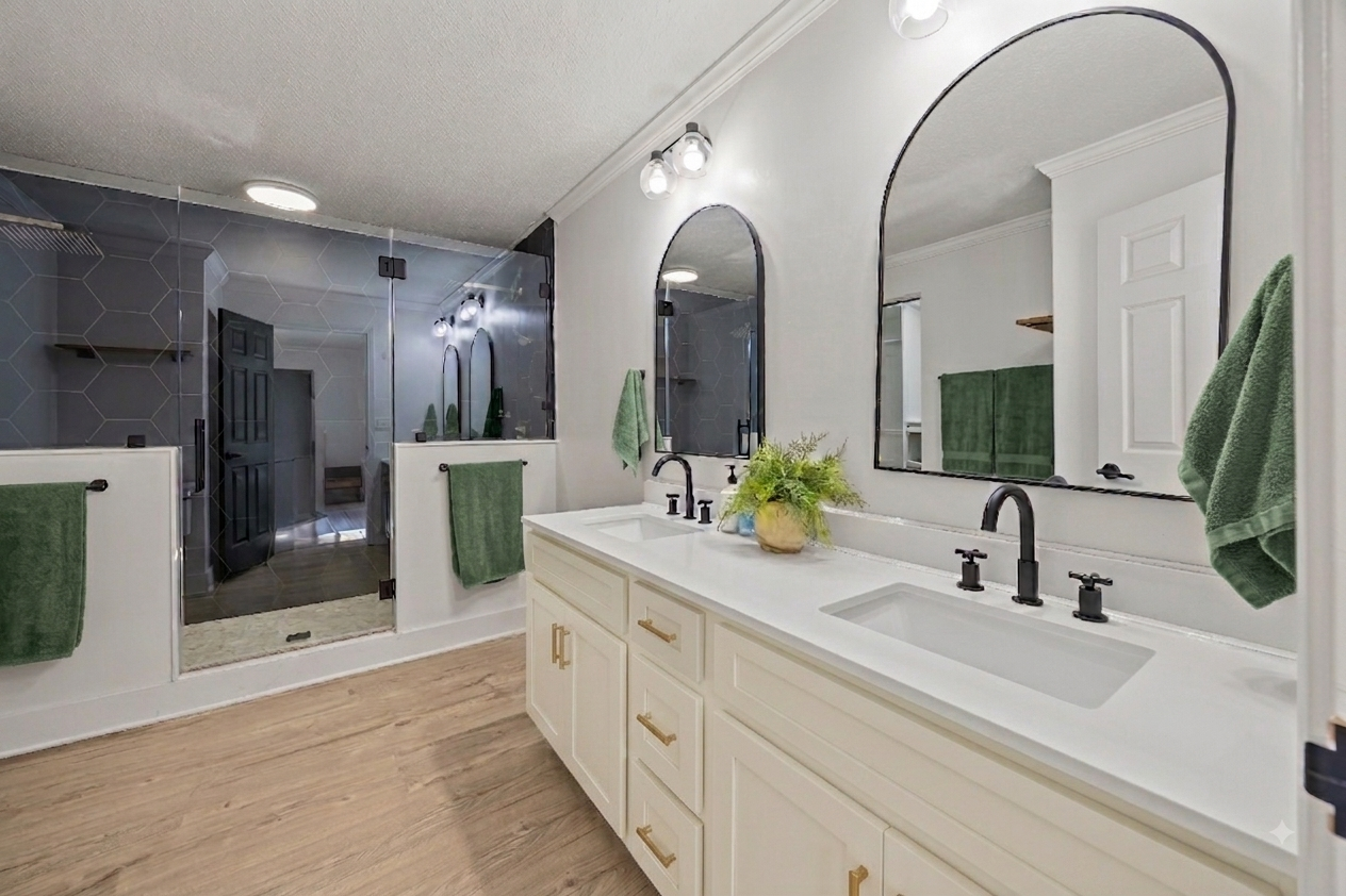 Bathroom with a double vanity, large mirrors, black fixtures, and a walk-in shower with a glass door and green towels.