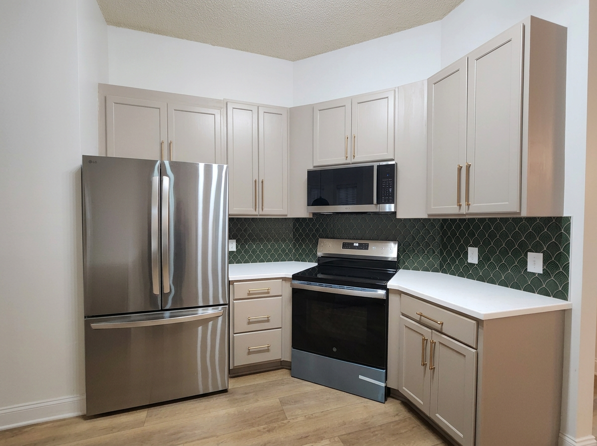 Kitchen with white cabinets, stainless steel appliances, and green patterned backsplash.