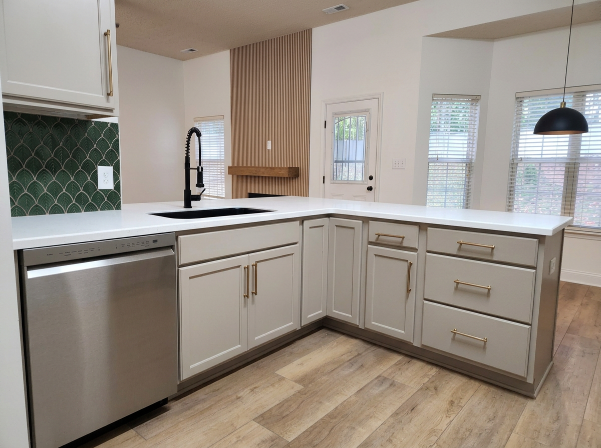 Modern kitchen with white cabinets, gold handles, white countertop, black faucet, stainless steel dishwasher, green patterned backsplash, wood flooring, and large windows with blinds.