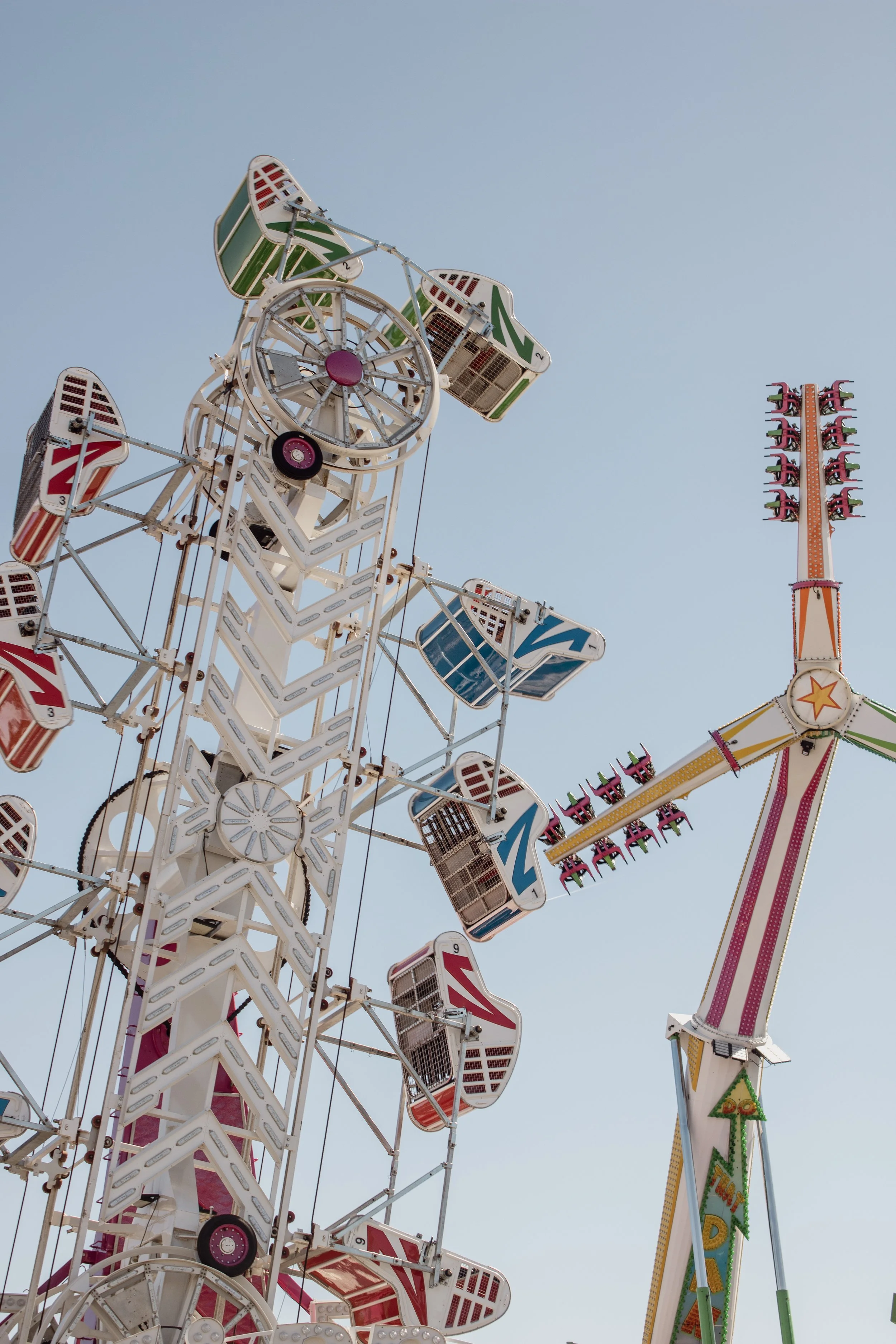 A Ferris wheel and a colorful ride at a fair against a clear blue sky.