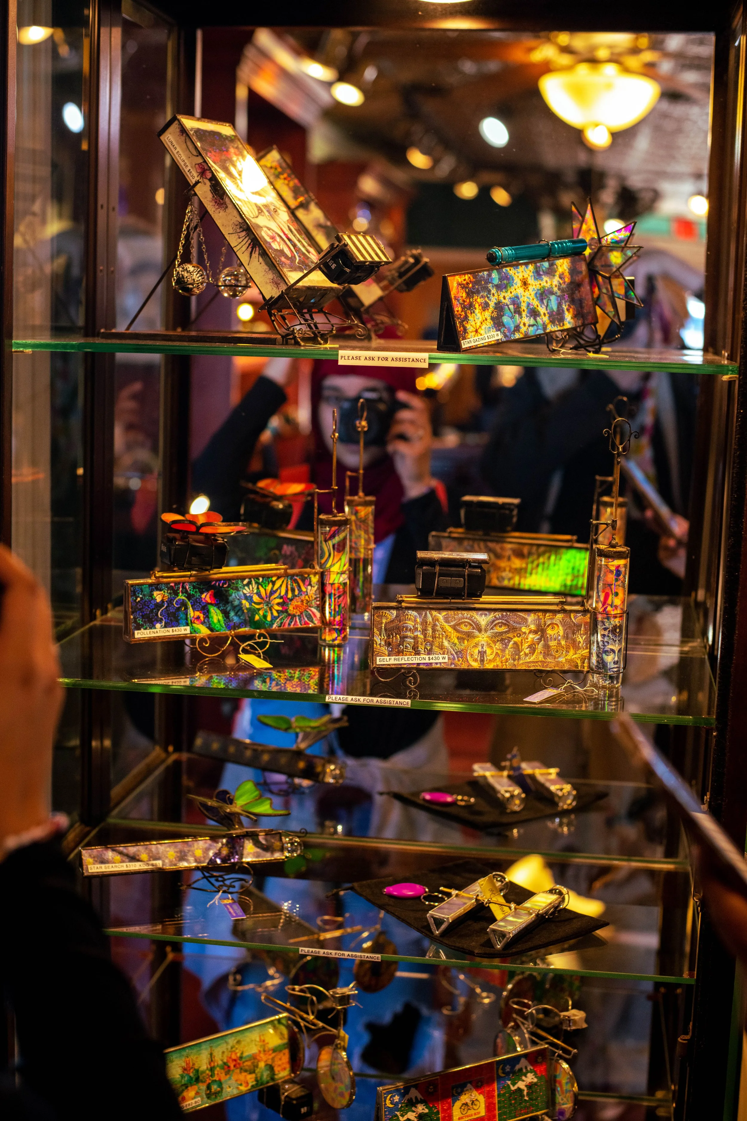 Displaycase with colorful, decorated jewelry and artwork, including brooches, pins, and small sculptures, in a dimly lit store or market setting.