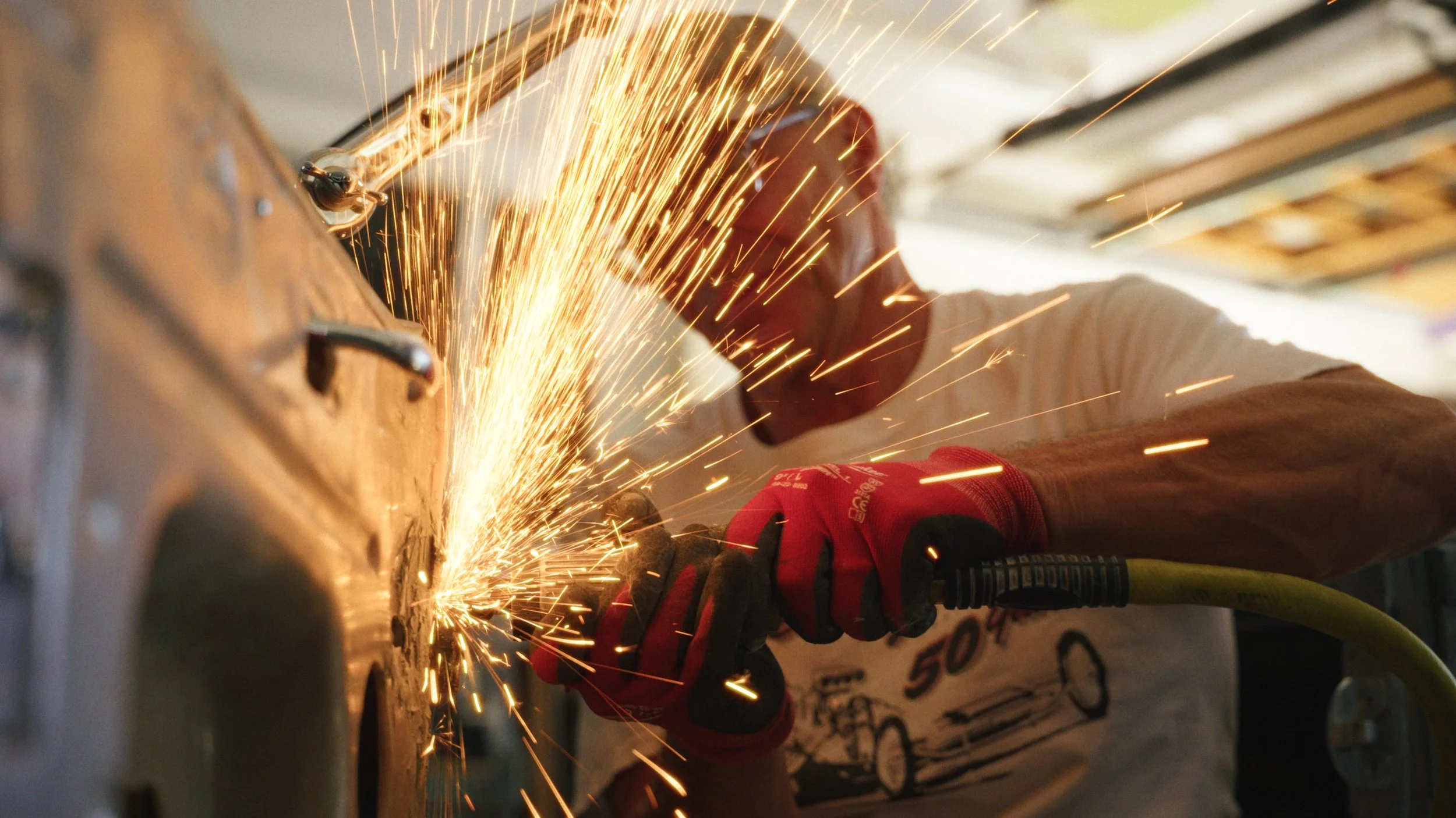 A person wearing red gloves welding metal, sparks flying.