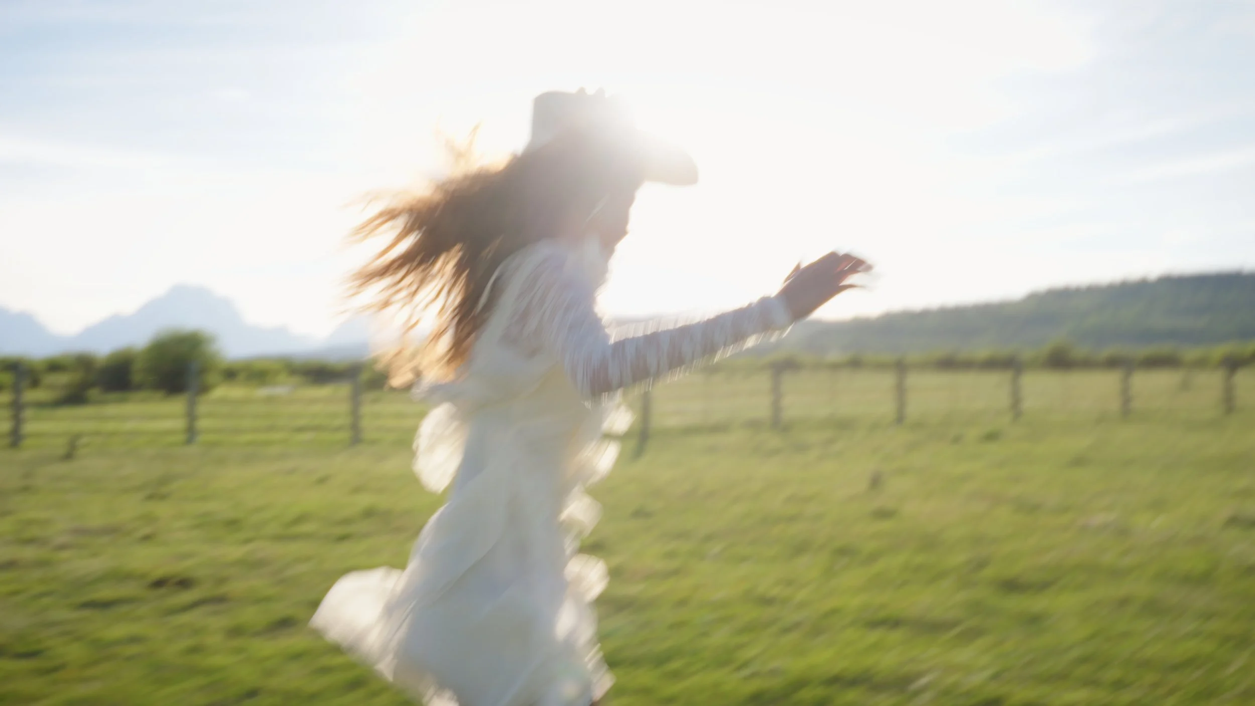 A person running outdoors in a grassy field during daytime, with the sun shining brightly behind them.