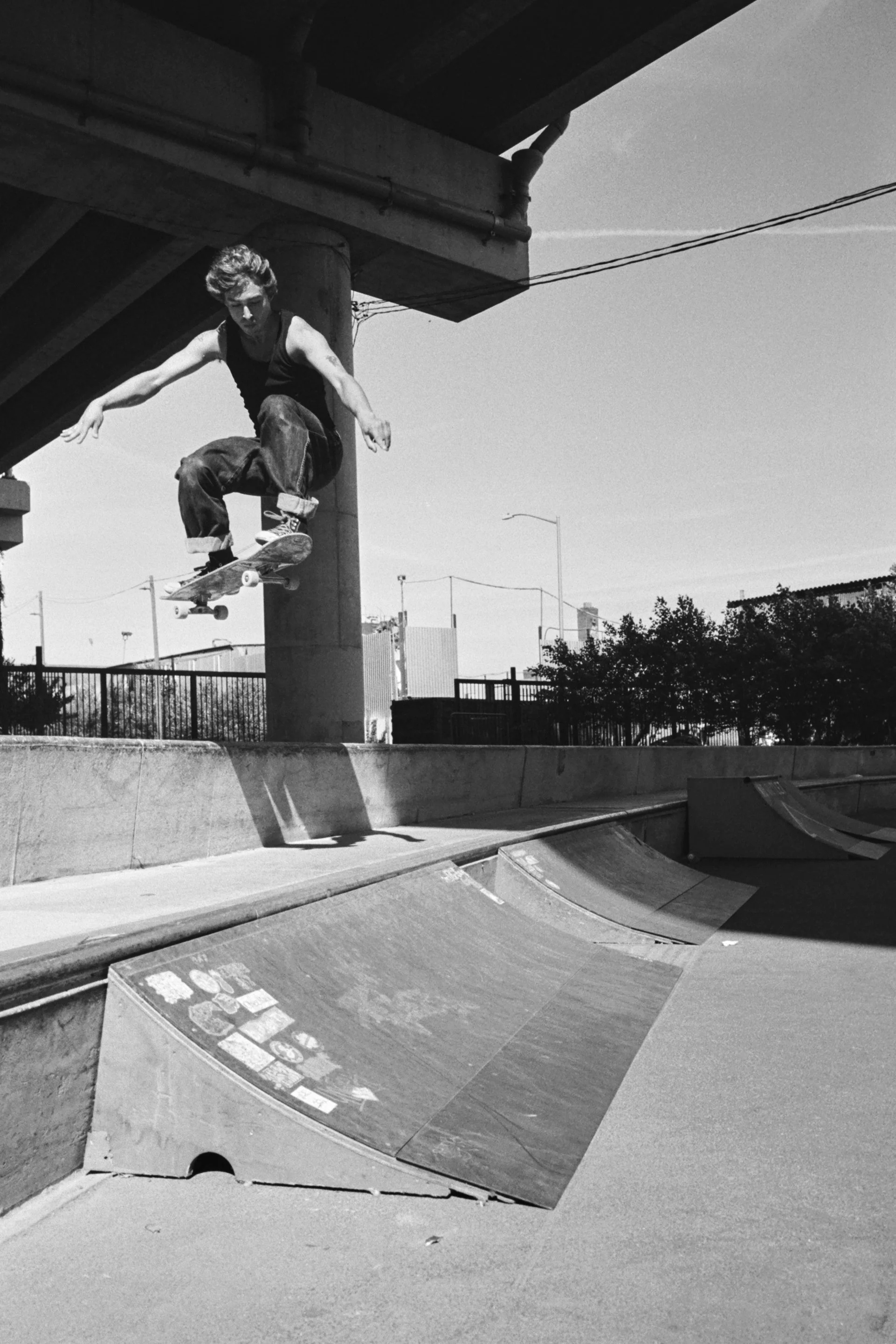 A skateboarder performing a trick at an outdoor skate park with ramps. The photo is in black and white.