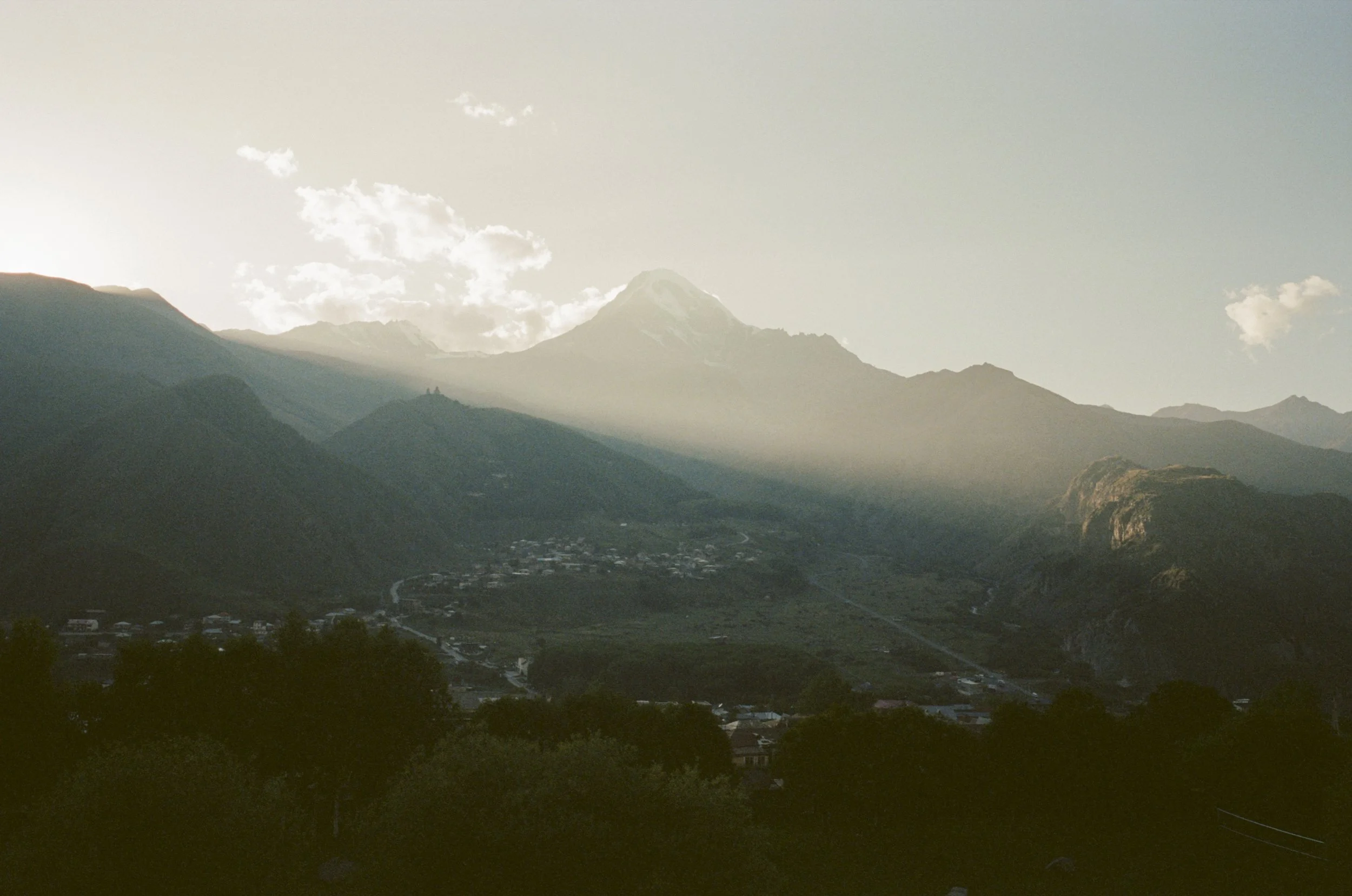 Scenic view of mountains with a snow-capped peak, clouds, and a small town in the valley during daylight.