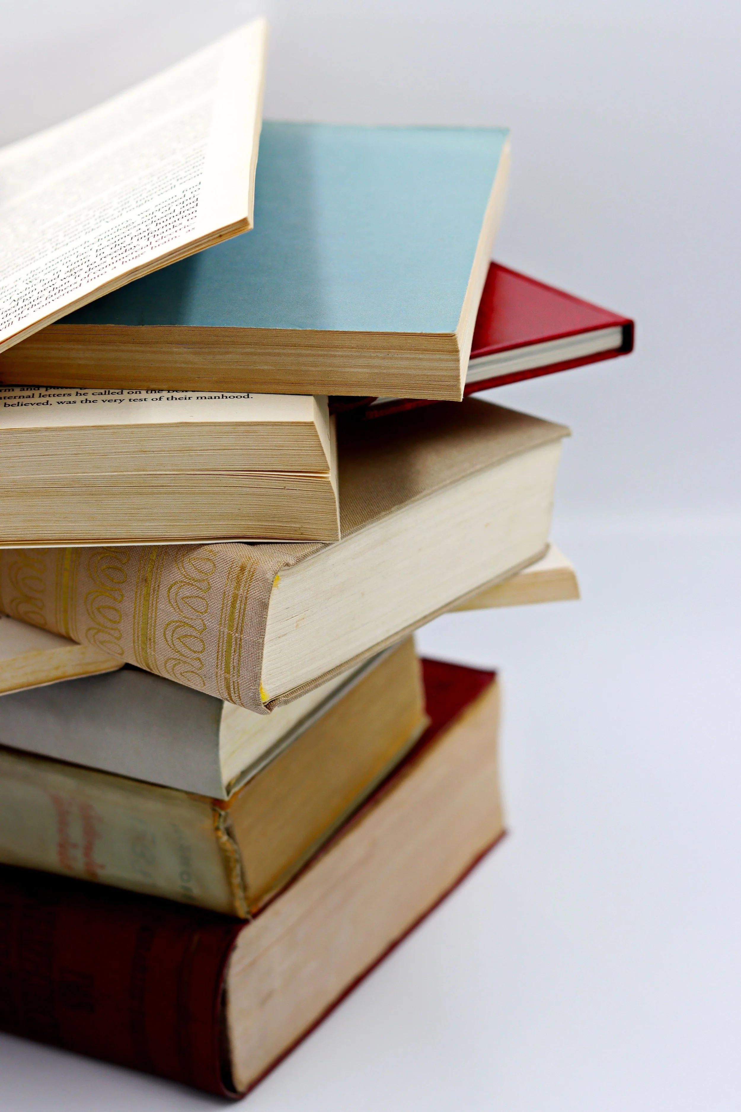 Stack of old books with varying colors, some with visible text on the spines, placed on a white surface.