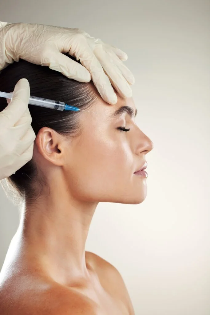 A woman receiving a cosmetic injection in her forehead from a medical professional wearing gloves.