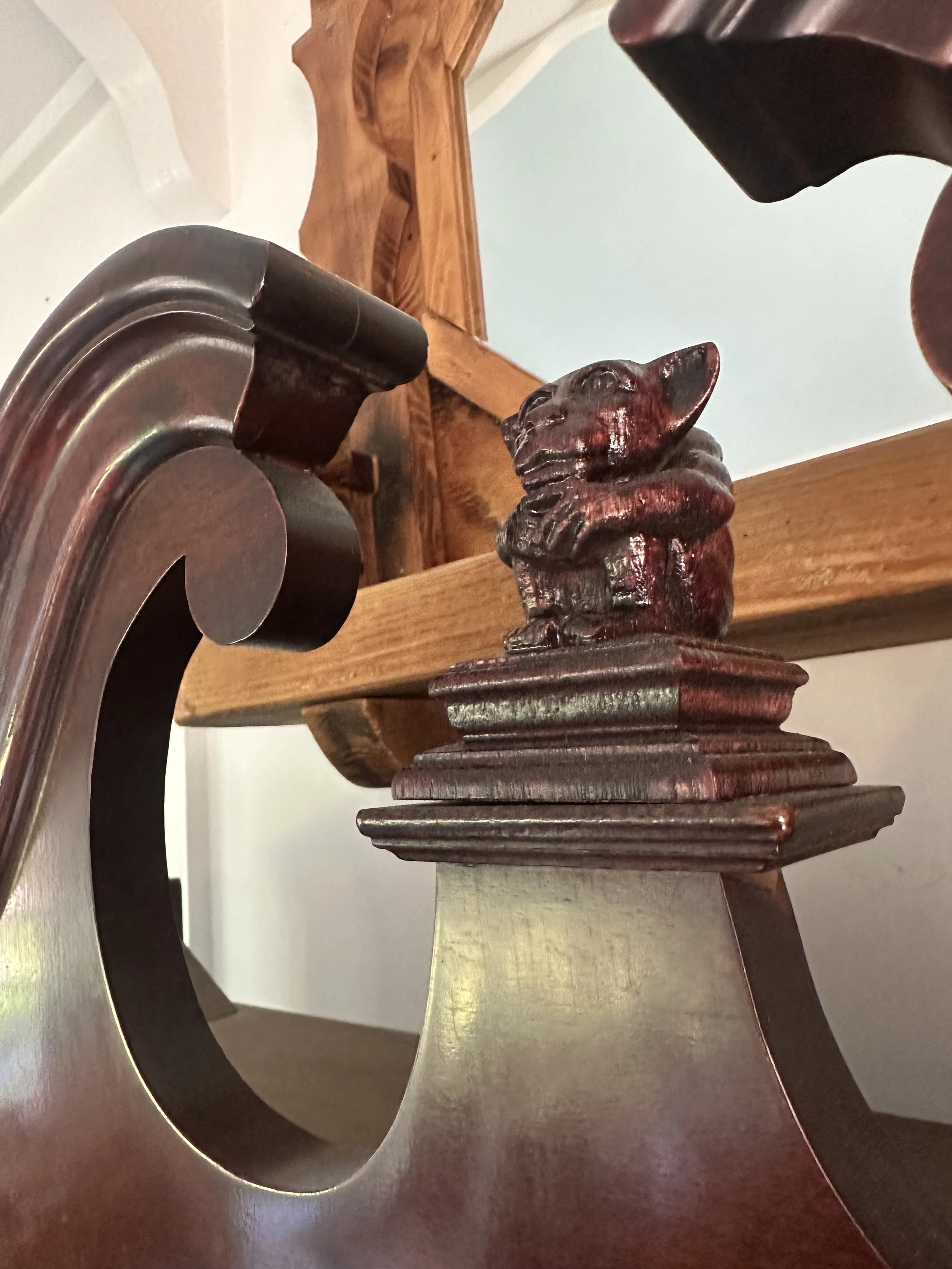 Close-up of wooden and metallic furniture pieces, including a carved wood figurine on a surface, a metal object with a curved and decorated design, and additional wooden and metallic components in the background.