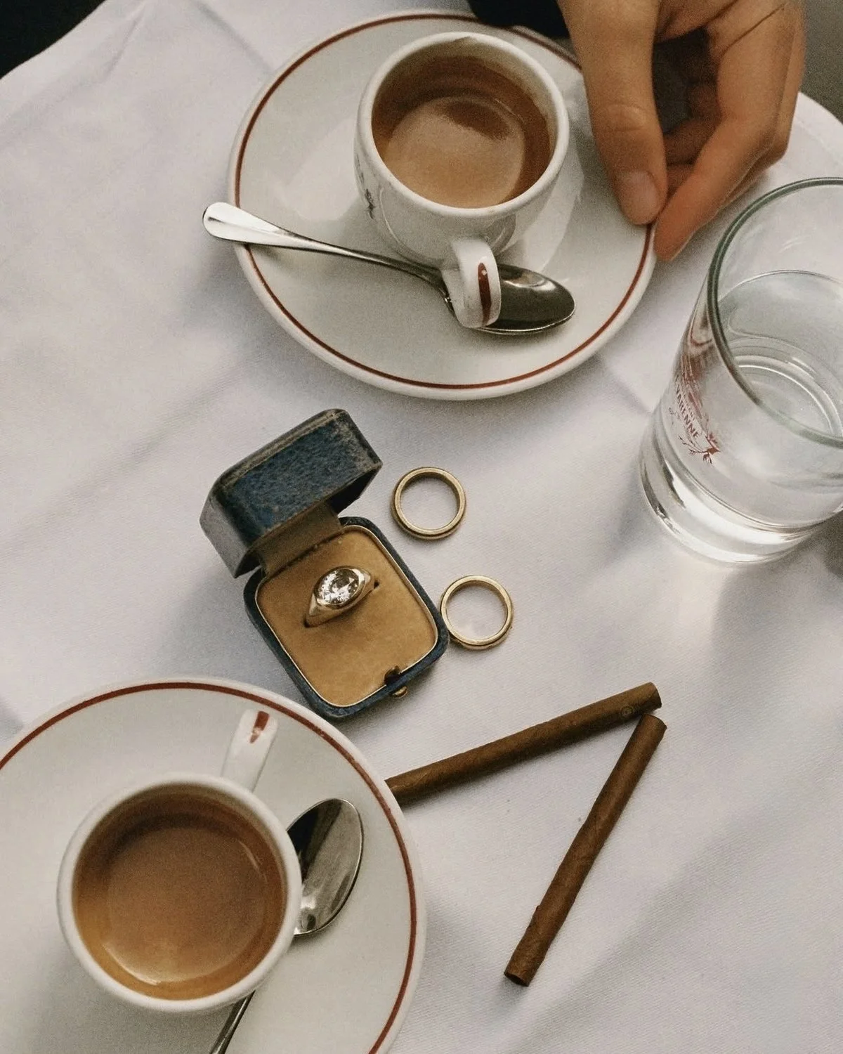 Two espressos beside wedding rings and an engagement ring on white linen