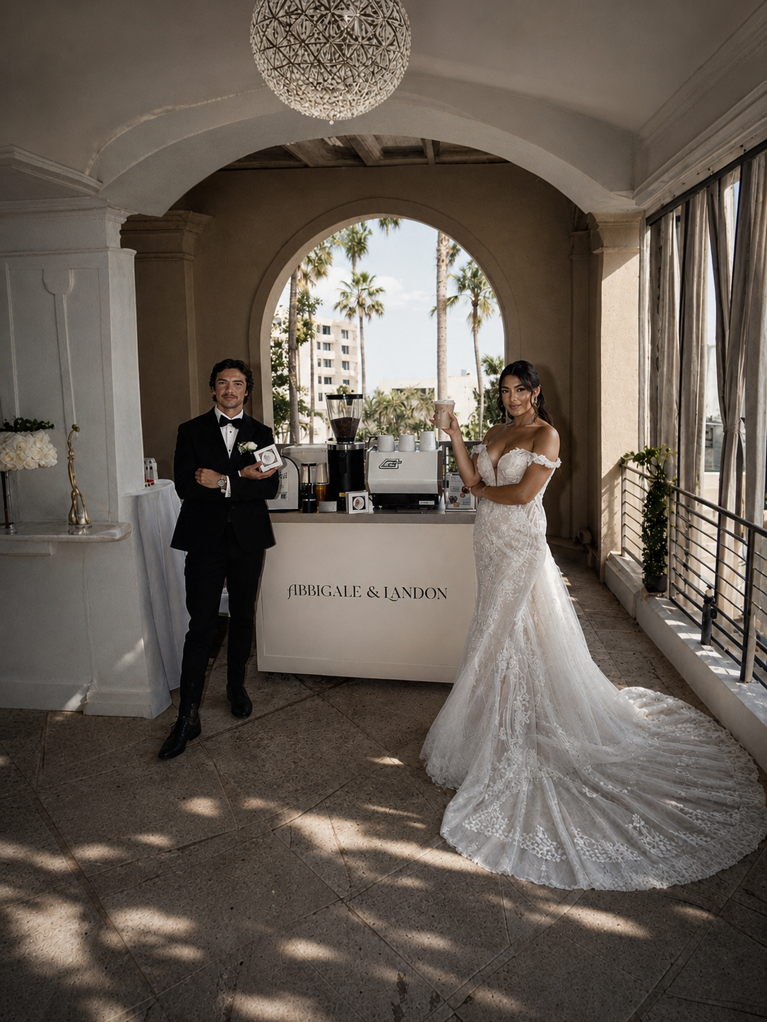 Bride and groom beside a custom Coffee At Your Wedding espresso bar under a palm-framed archway