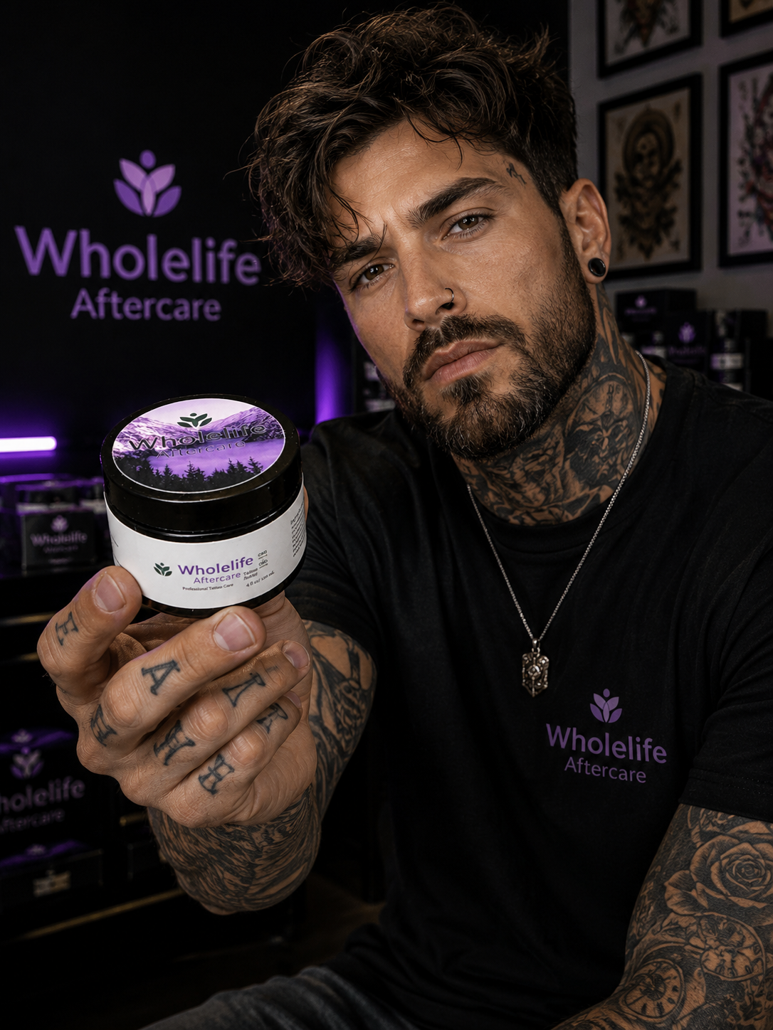 A man with tattoos and pierced ears holding a container of Wholelife Aftercare product in front of a dark background with Wholelife Aftercare branding