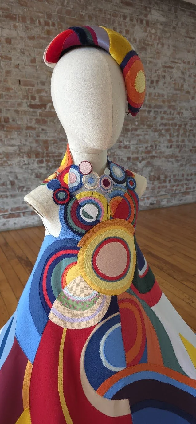 A child mannequin dressed in a colourful, abstract, circular-patterned outfit with a matching headwrap, all featuring vibrant concentric circle designs.