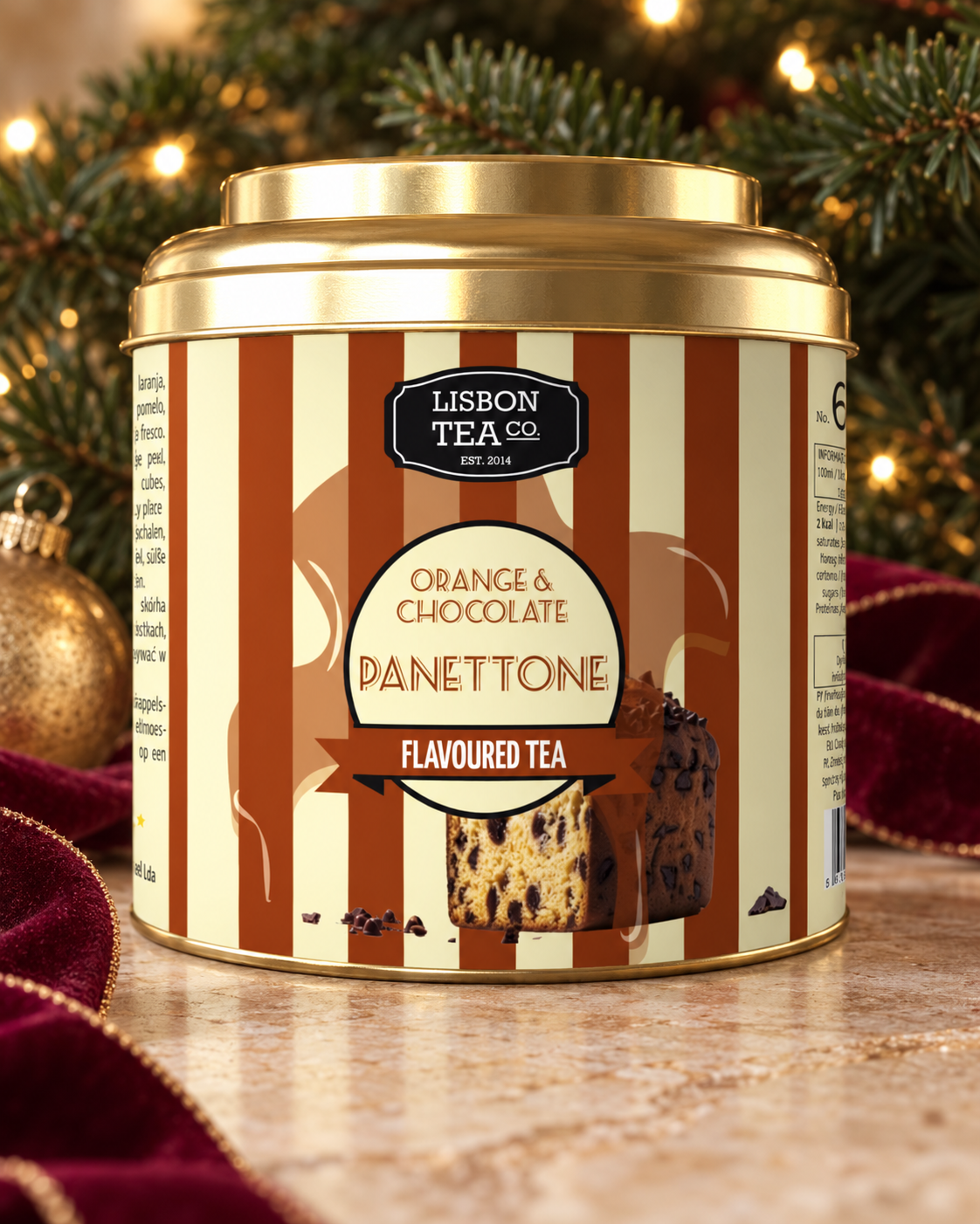 Lata dourada de chá de sabores de laranja e chocolate com imagem de panetone na embalagem, decorada com enfeites natalinos ao fundo.
