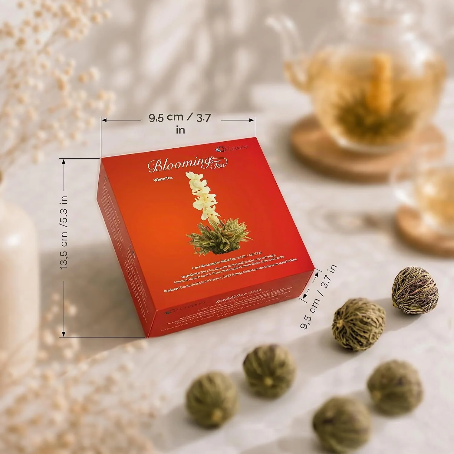Caixa de flores de chá Creano com esferas de chá para infusão, junto de uma chávena de vidro.