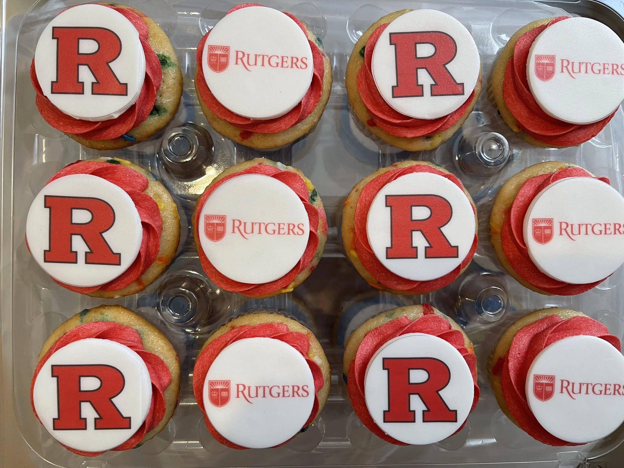 Celebratory cupcakes with red and white frosting, topped with edible images of the Rutgers University logo and a large red letter 'R'.