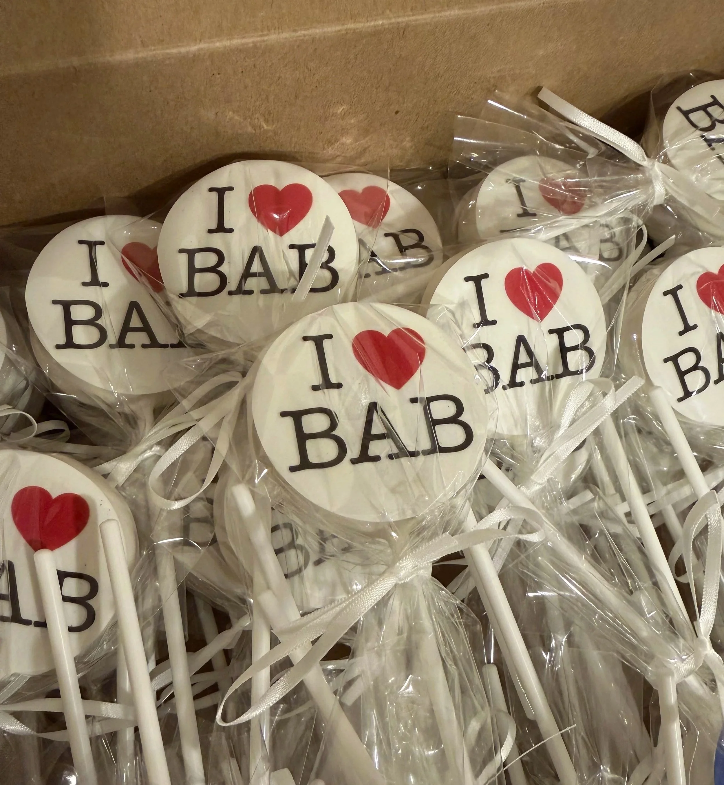 Multiple round lollipops with white background and black text that says "I ♥ BABY DADDY" and red heart symbol, each wrapped in clear plastic and attached to white sticks.