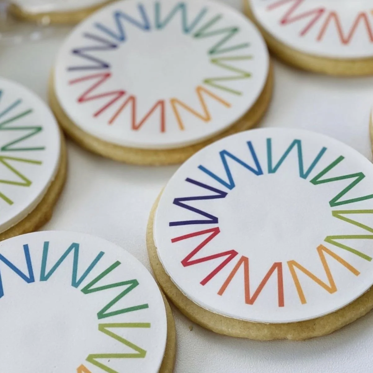 Decorative cookies with a white base and a rainbow-colored circular pattern of zigzag lines.