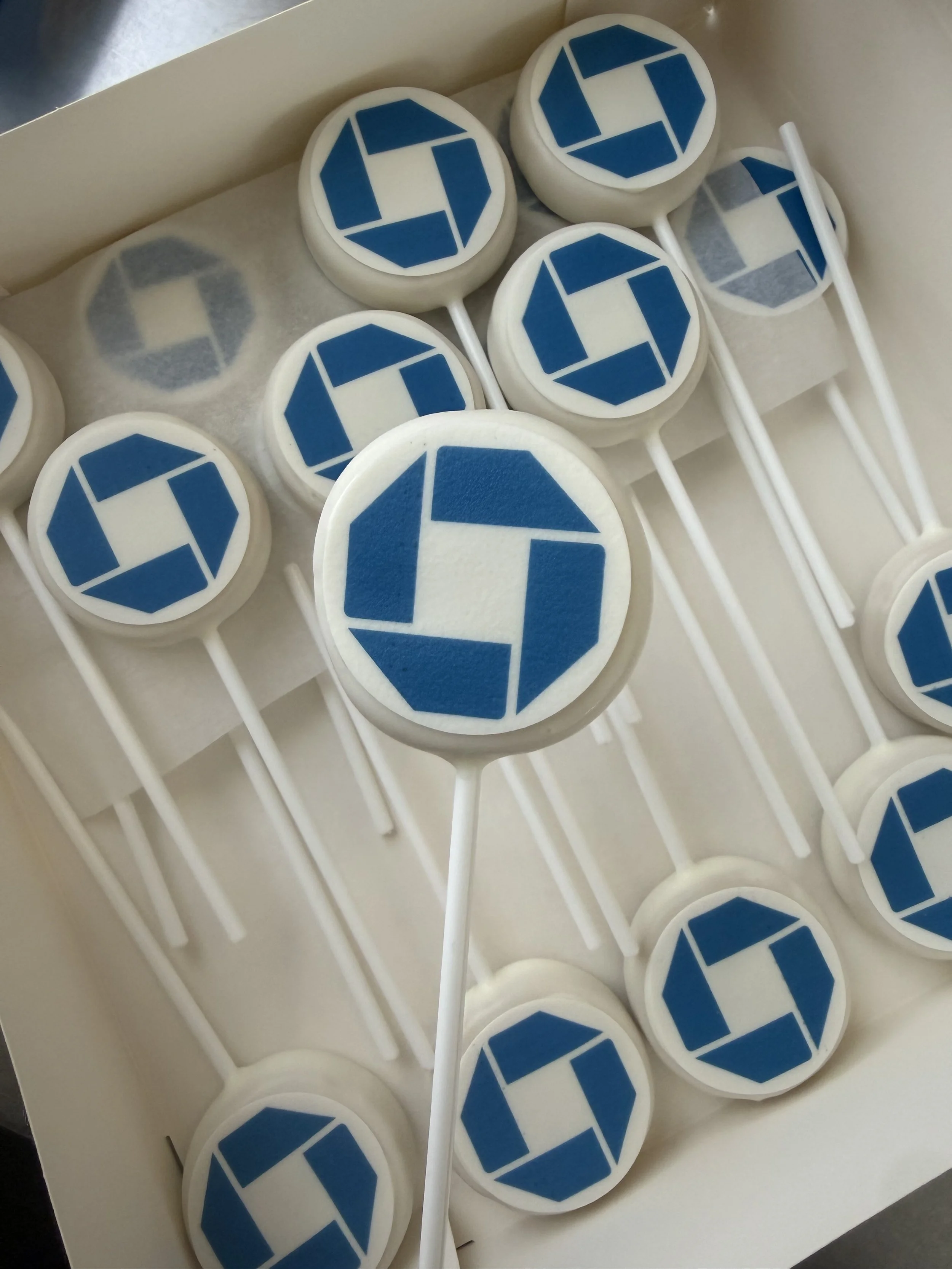 Collection of white lollipops with blue geometric logo on top, arranged in a box with white paper lining.