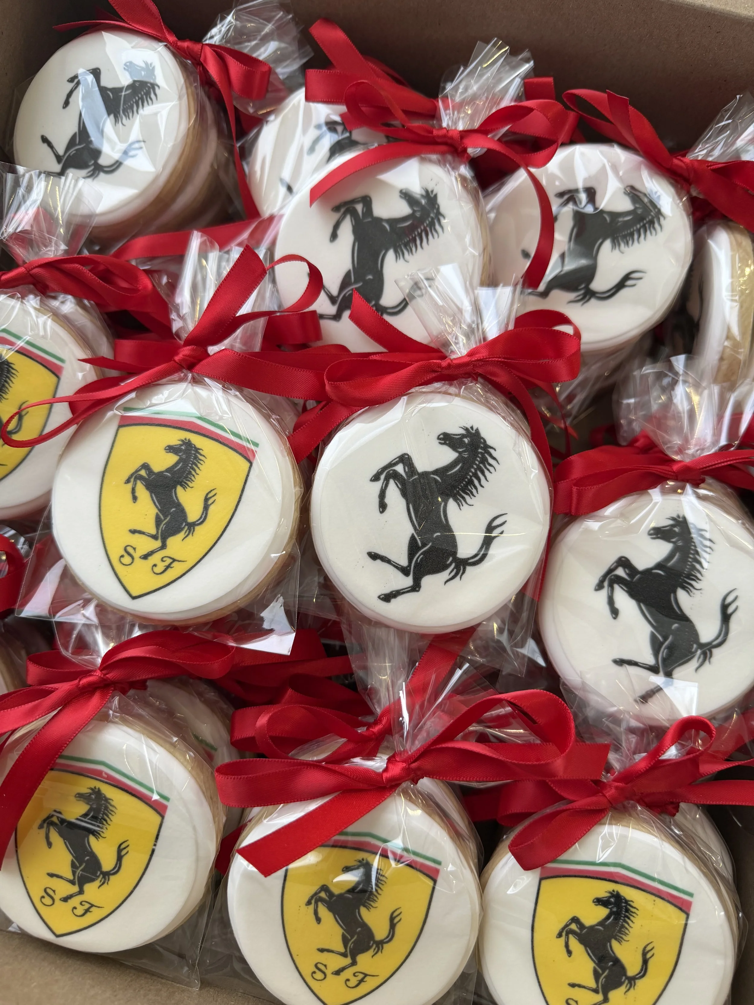 Cookies decorated with Ferrari logo, wrapped in clear plastic with red ribbons.