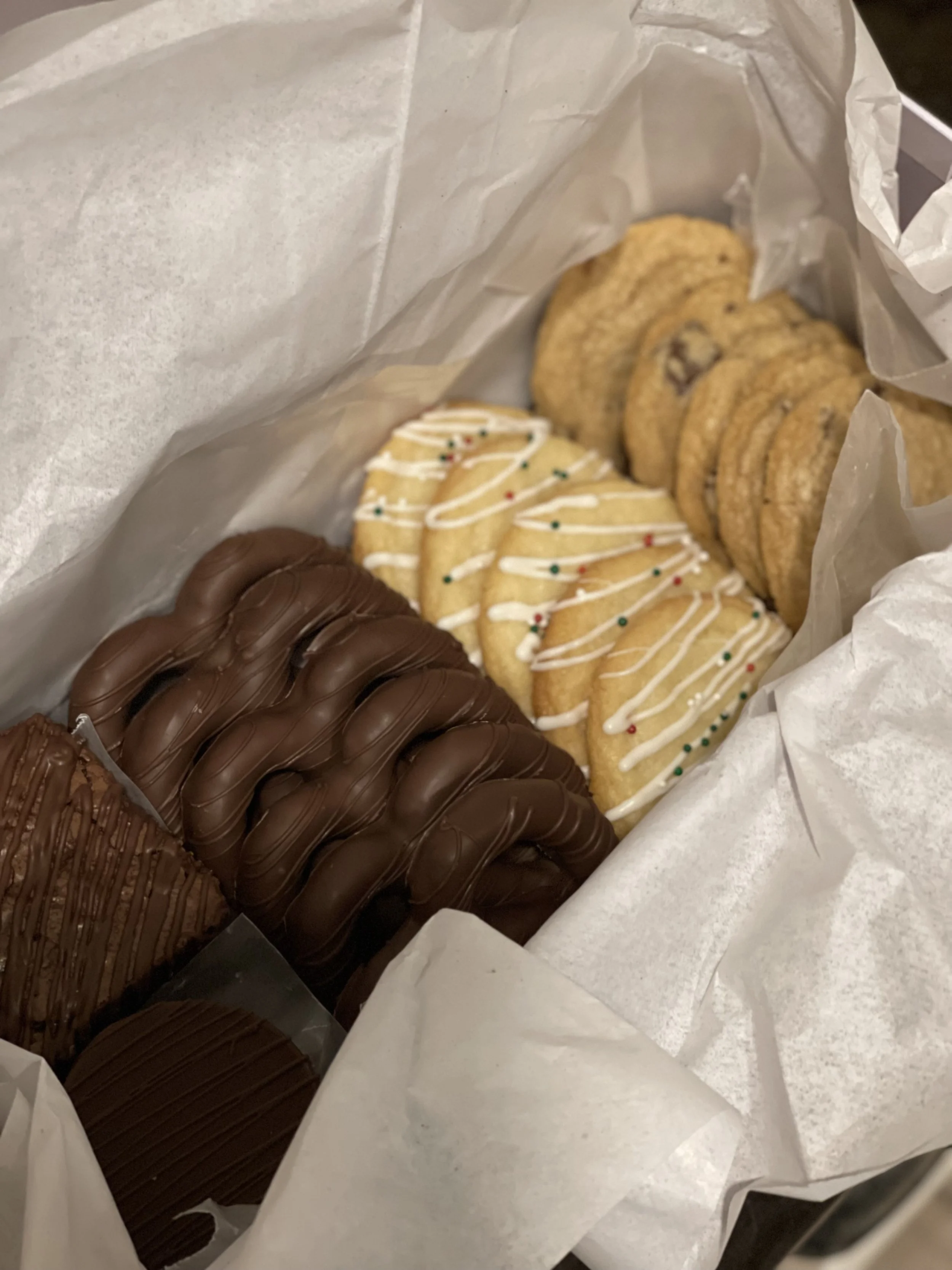 Assorted cookies, including chocolate and sugar cookies, inside a white paper bag.