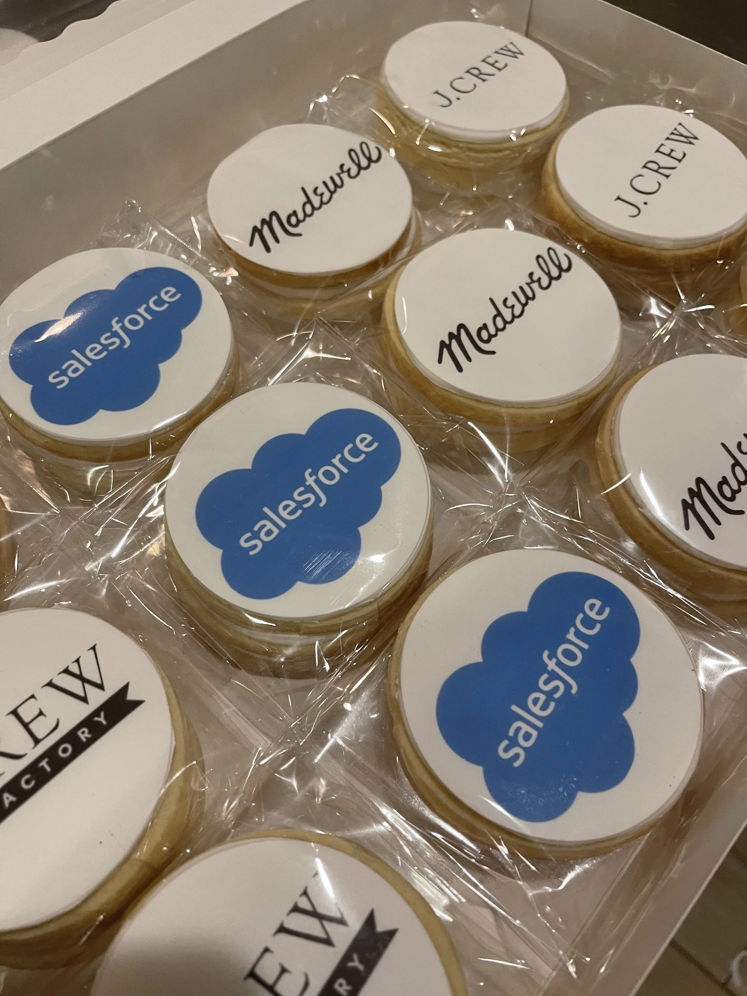 Assorted cookies in clear plastic wrapping, featuring logos of 'Salesforce' and 'J.Crew', on a white background with some black text.