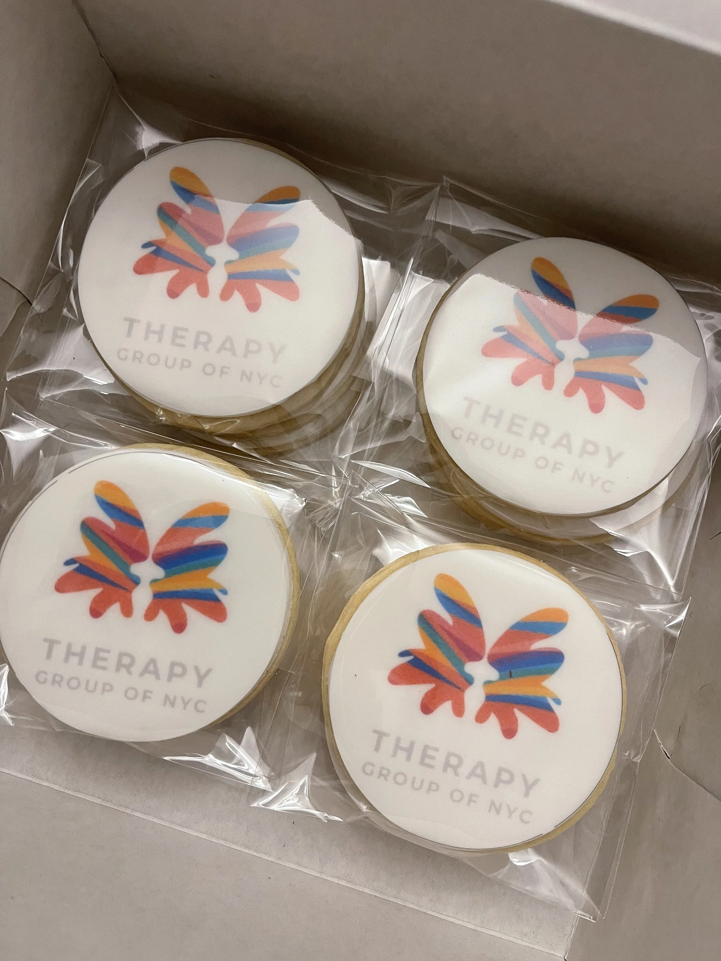 Cookies with a colorful butterfly logo and the text 'THERAPY GROUP OF NYC' on top, packaged in clear plastic inside a brown box.