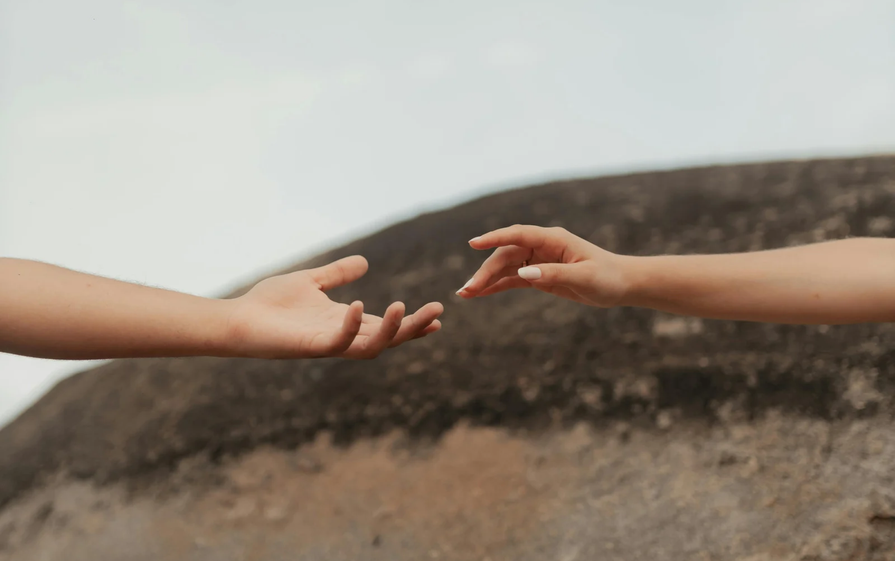 Two hands reaching towards each other with fingers almost touching, set against a simple background.