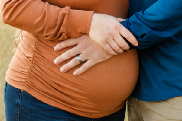 Close-up of a pregnant woman and partner holding her belly outdoors.