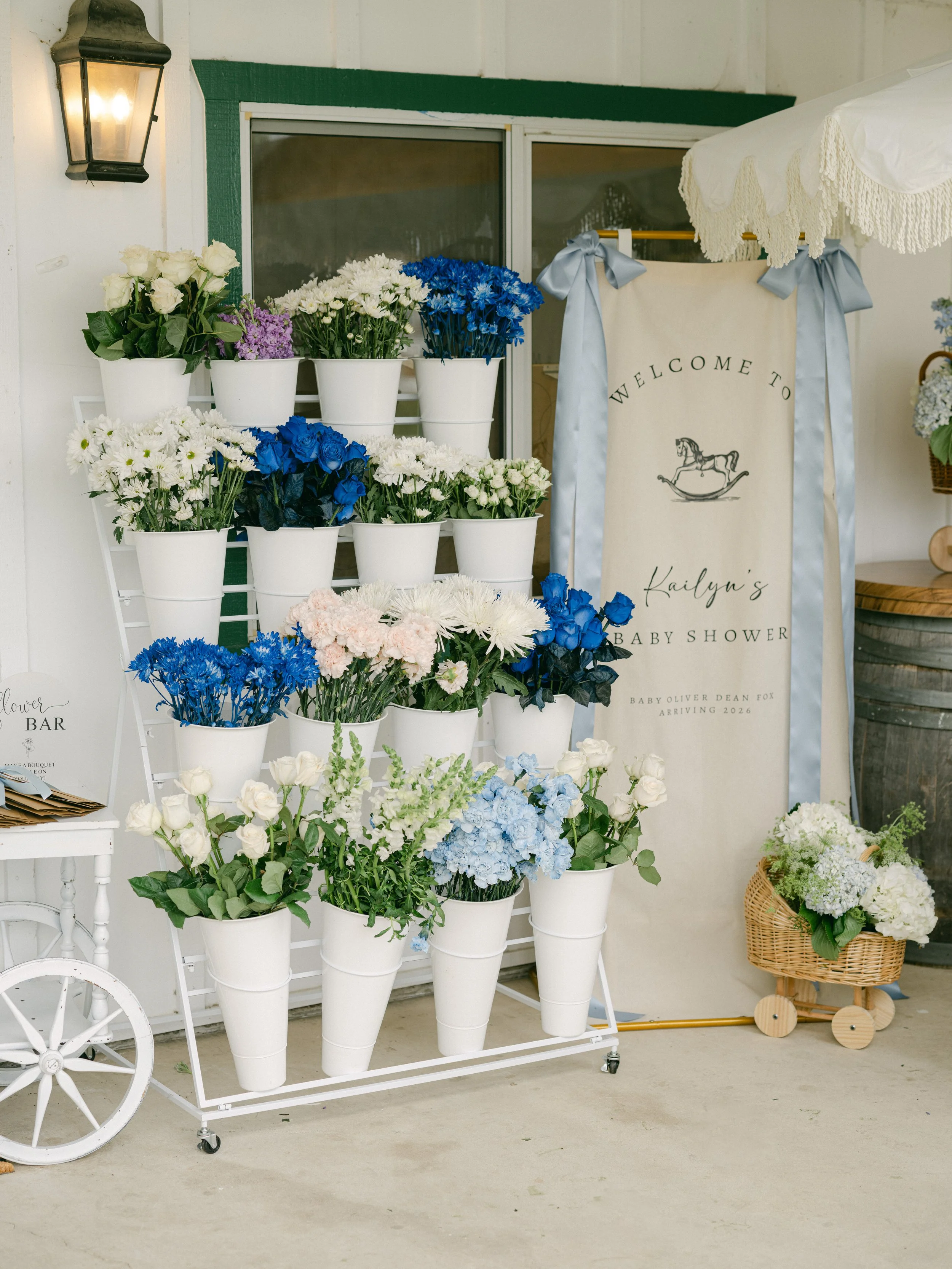 White floral stand with white and blue flowers near a wedding or baby shower sign that says "Welcome to Kailyn's Baby Shower."