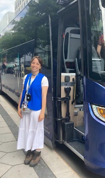 A woman standing next to a modern blue and black bus on a city street, smiling at the camera.