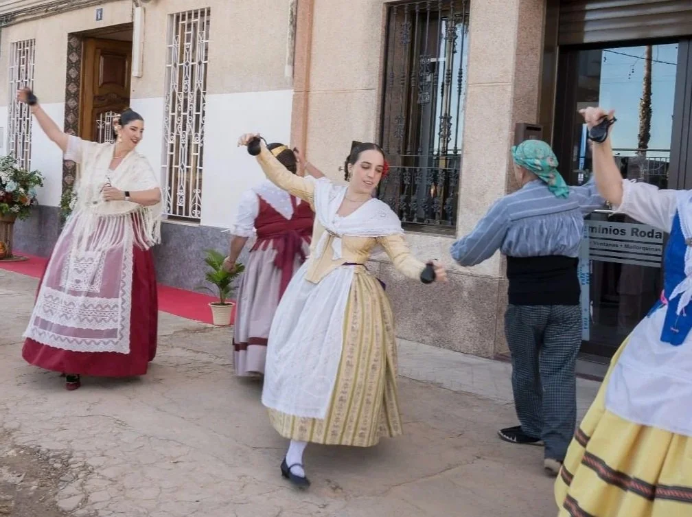 Women and men dressed in traditional clothing dancing outdoors in a festive setting, possibly celebrating a cultural event.