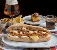 Hot dog with mustard on a bun, alongside potato chips, and a glass of dark soda with ice on a table.