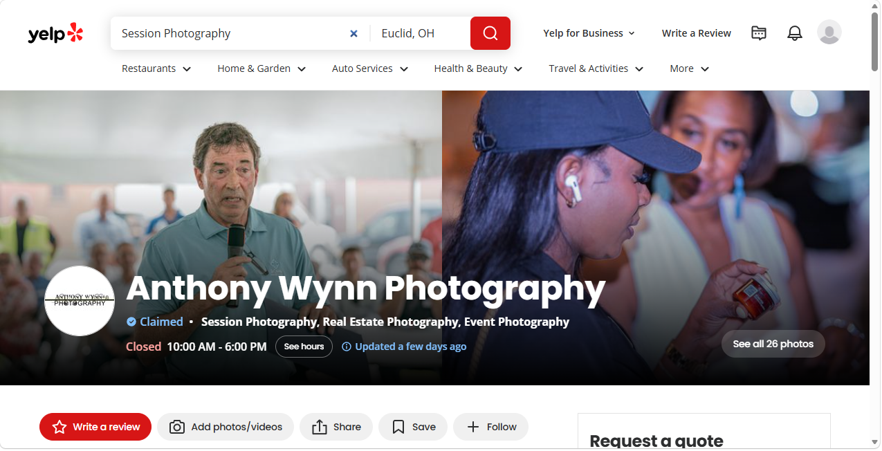 Yelp profile page for Anthony Wynn Photography with a banner photo showing a man speaking into a microphone at an outdoor event and a woman in a black cap holding a small container, with a blurred background of people.