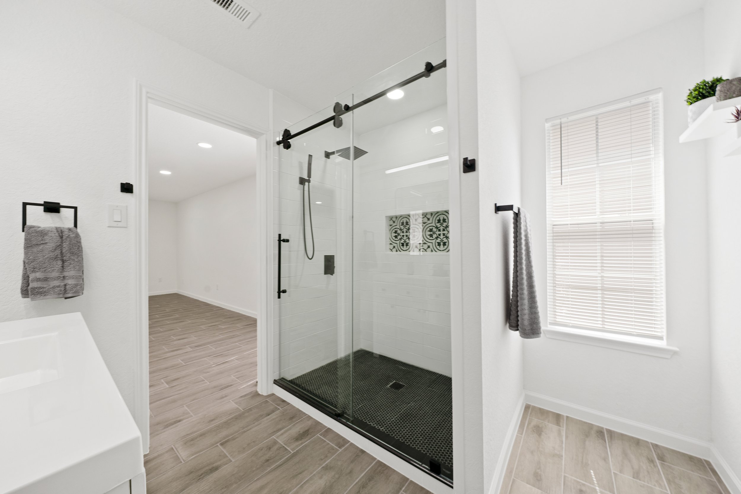 Modern bathroom with a glass shower enclosure, a window with blinds, and towel racks on white walls.