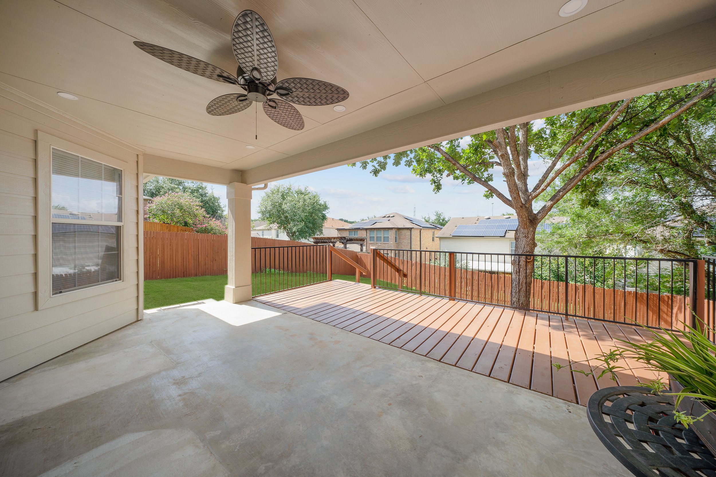Covered backyard patio with a ceiling fan, window, and a view of trees, solar panels, and neighboring houses.