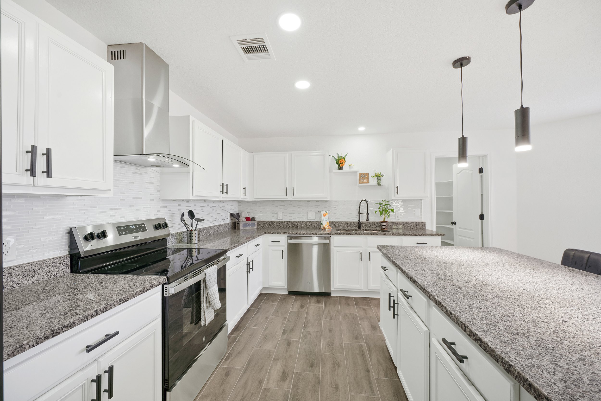Modern kitchen with white cabinets, stainless steel appliances, granite countertops, and pendant lighting.