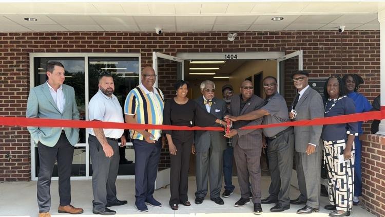 Group of people attending a ribbon-cutting ceremony outside a building, with some holding scissors.