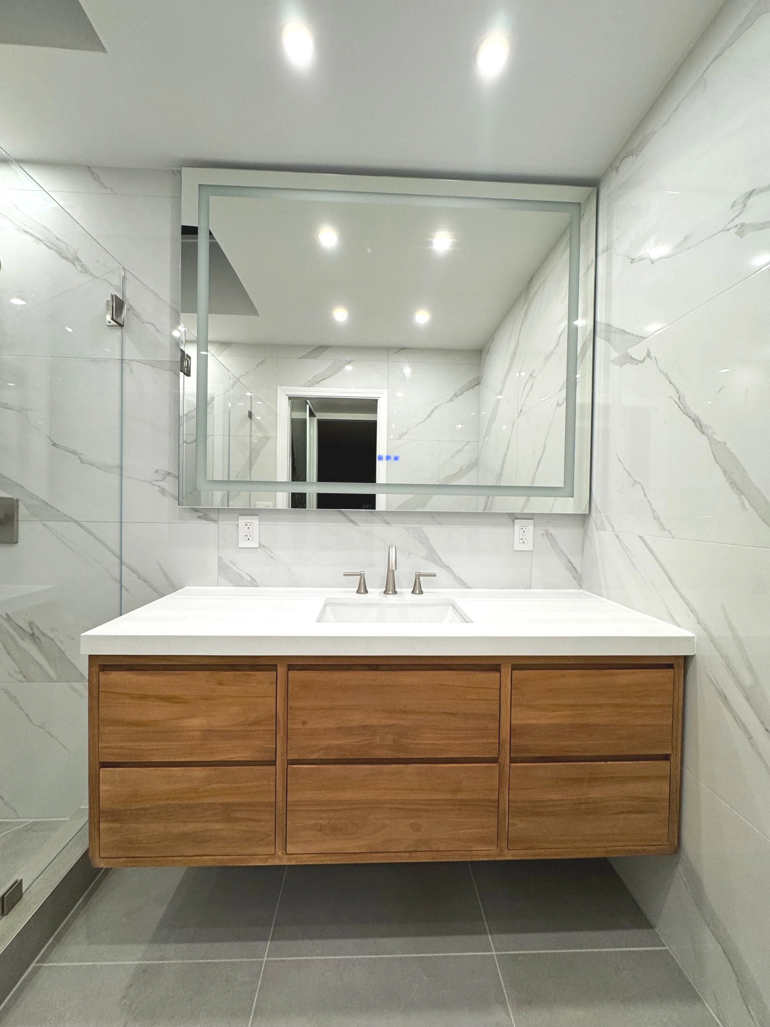 Modern bathroom vanity with a white countertop, wooden cabinets, and a large rectangular mirror.