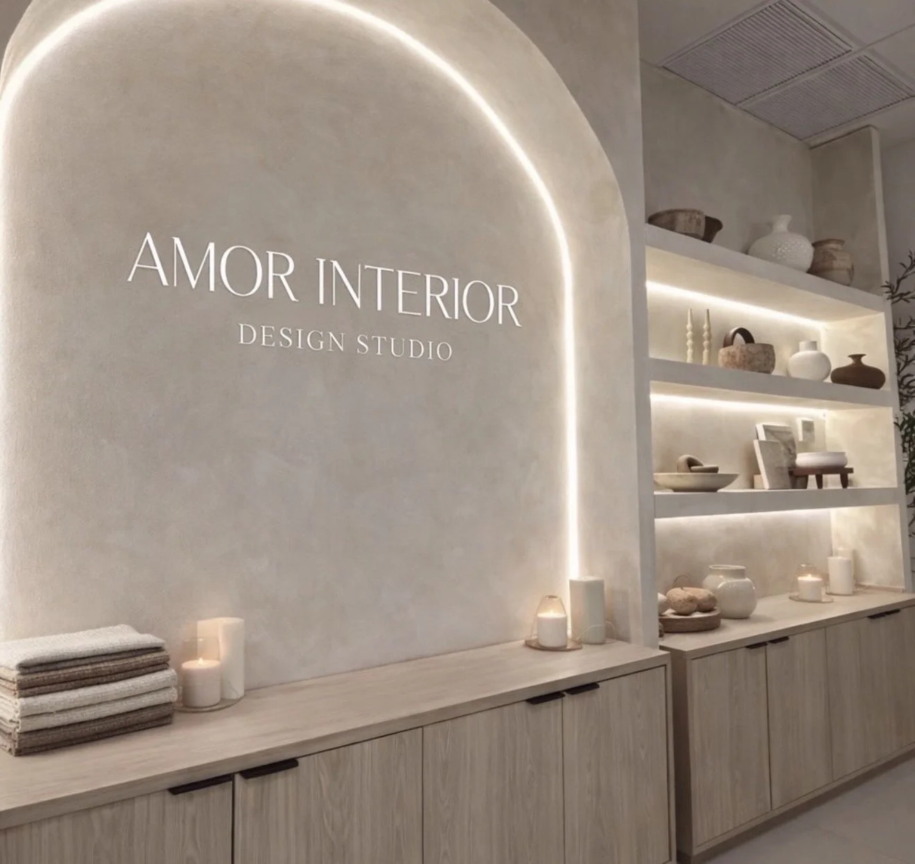 Interior of a design studio named Amor Interior, featuring a minimalist decor with shelves of ceramic vases and decorative objects, illuminated by soft lighting, with a sign on the wall reading Amor Interior Design Studio.