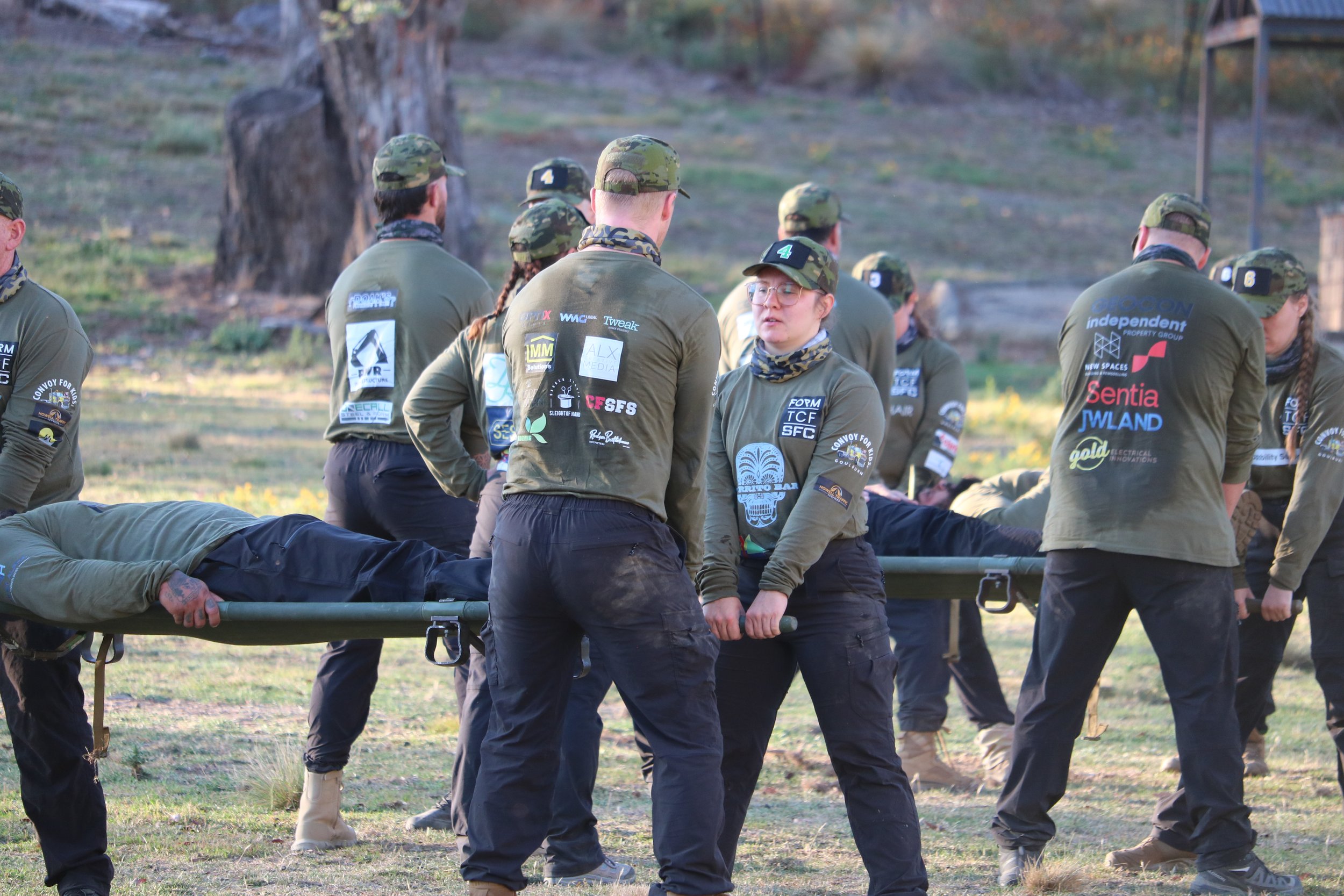 A30 Unbroken participants gathered outdoors in a grassy area with trees, participating in a team activity carrying a stretcher with a person on it.