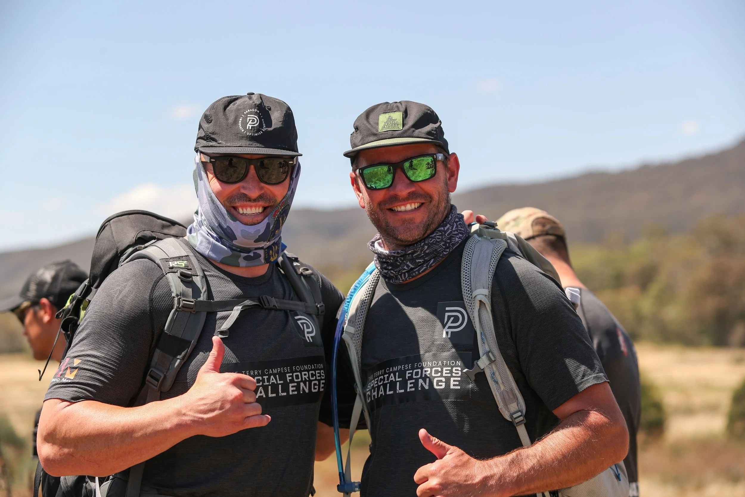 Terry Campese and Jeremy Howell smiling wearing hiking gear and sunglasses, standing outdoors with a mountainous background, participating in the Terry Campese Foundation Special Forces Challenge.