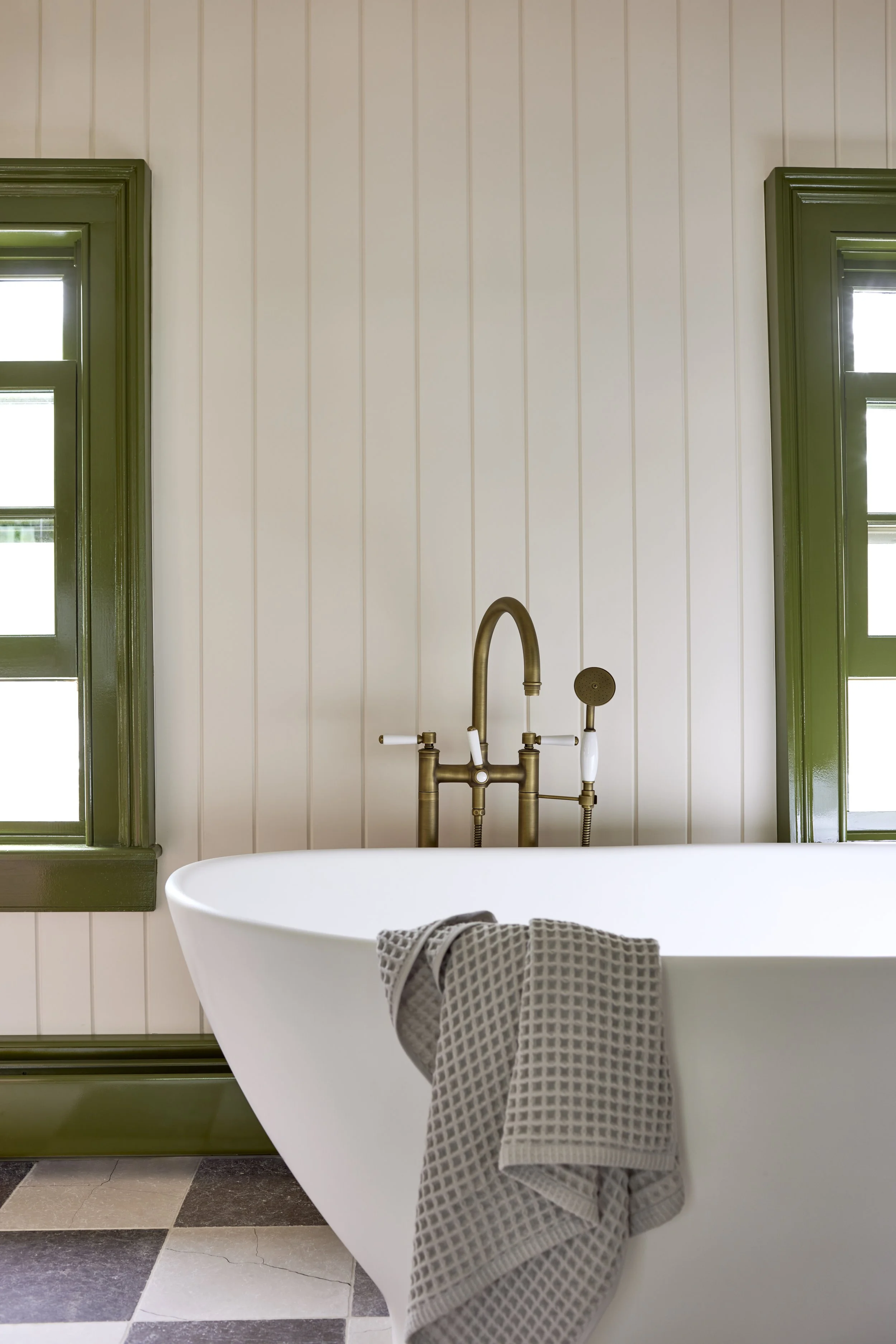 white tub with brass hardware and windows with bright green molding in the background