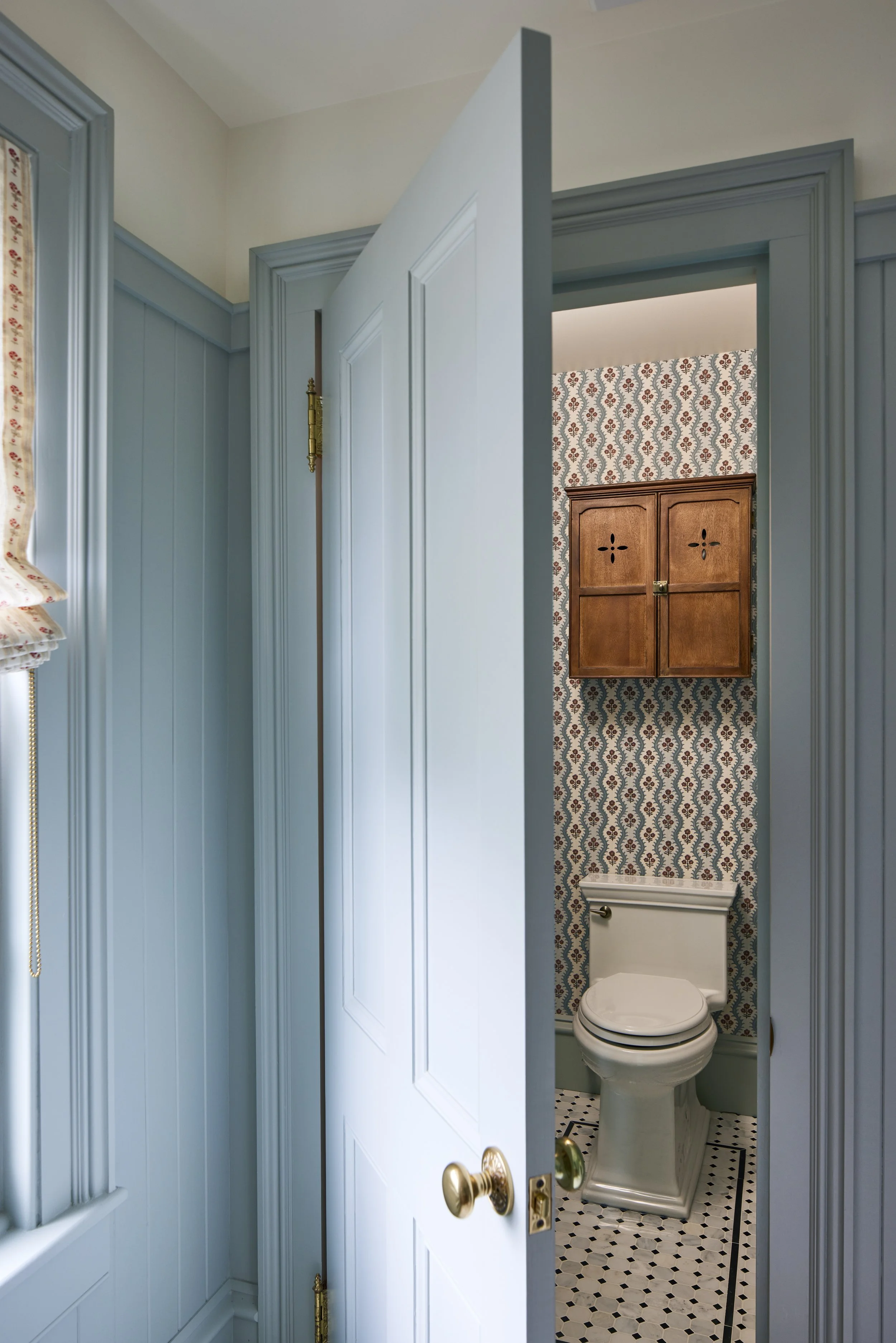 blue door slightly ajar showing white toilet with decorative wallpaper in background