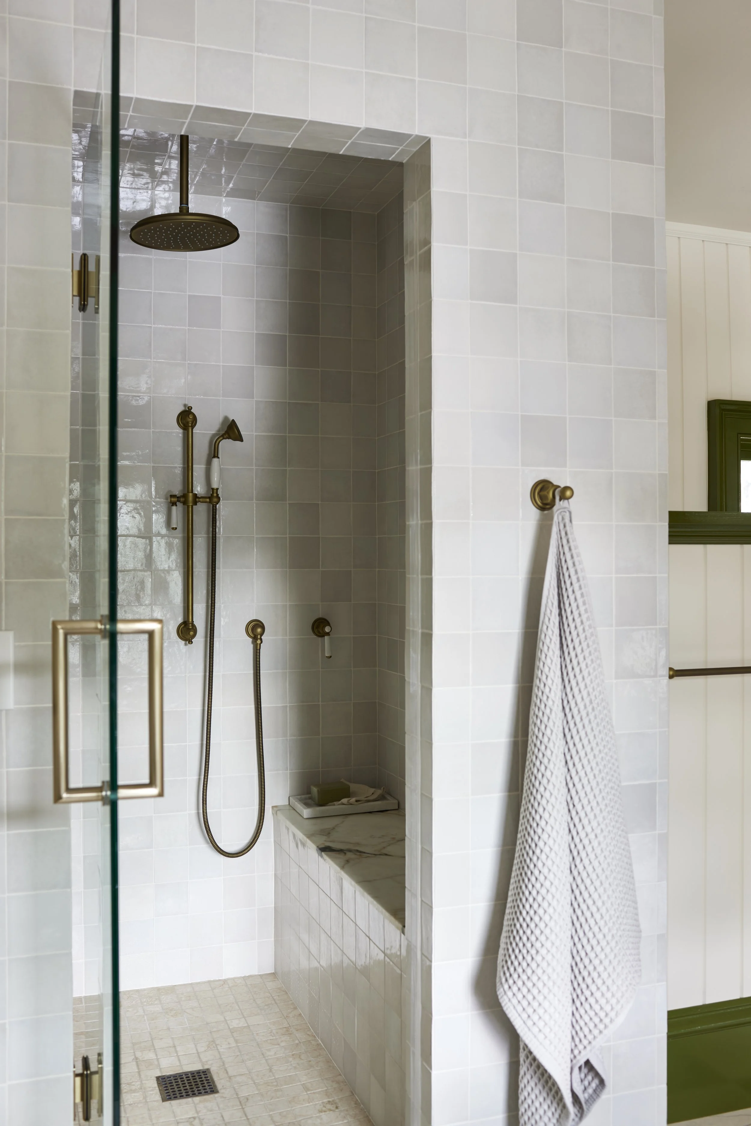 standing shower with light colored tiles and brass hardware