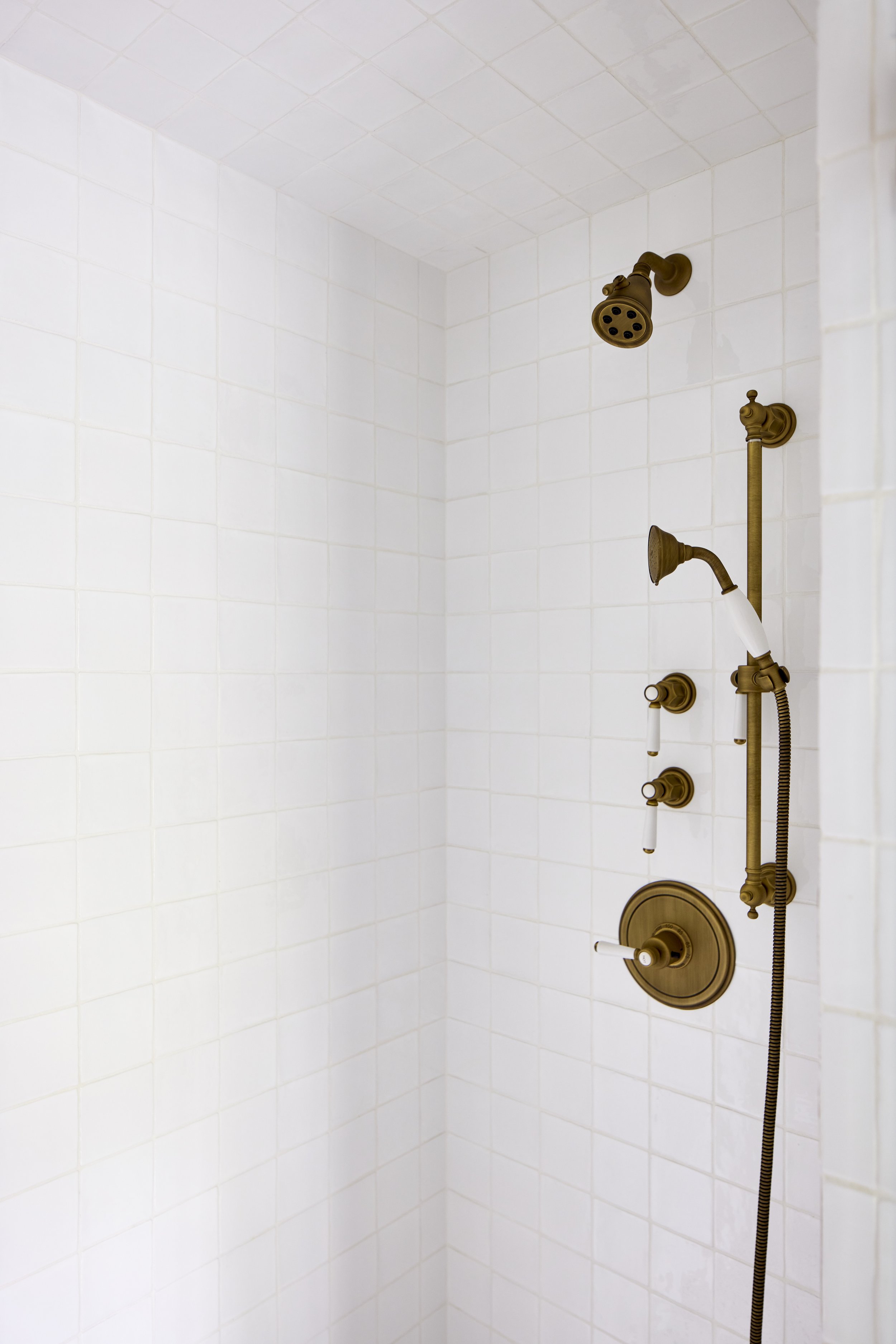 interior of white tile standing shower with brass showerhead and hardware