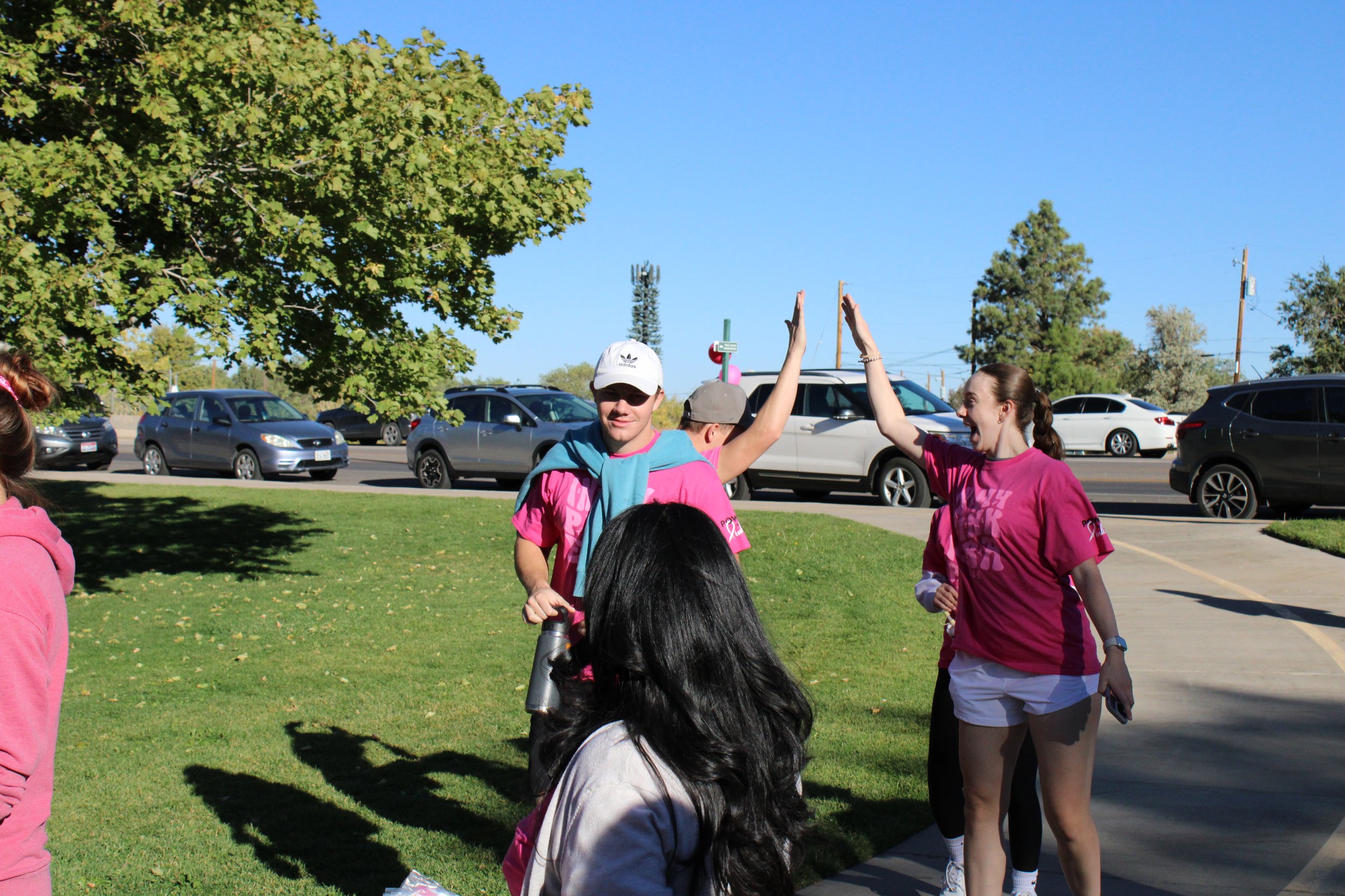 People participating in a high-five outdoors near parked cars and trees.